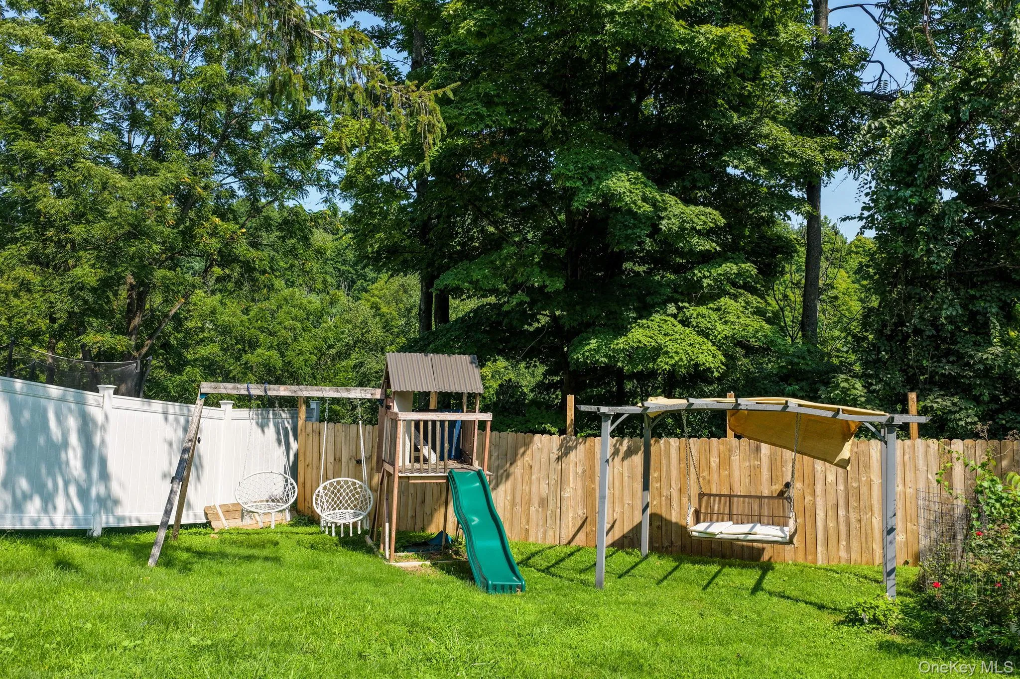 Expansive backyard oasis featuring mature tree canopy, lush lawn, wooden play structure with slide, swing set, and sandbox—ideal for outdoor recreation and entertainment Expansive backyard oasis featuring mature tree canopy, lush lawn, wooden play structure with slide, swing set, and sandbox—ideal for outdoor recreation and entertainment