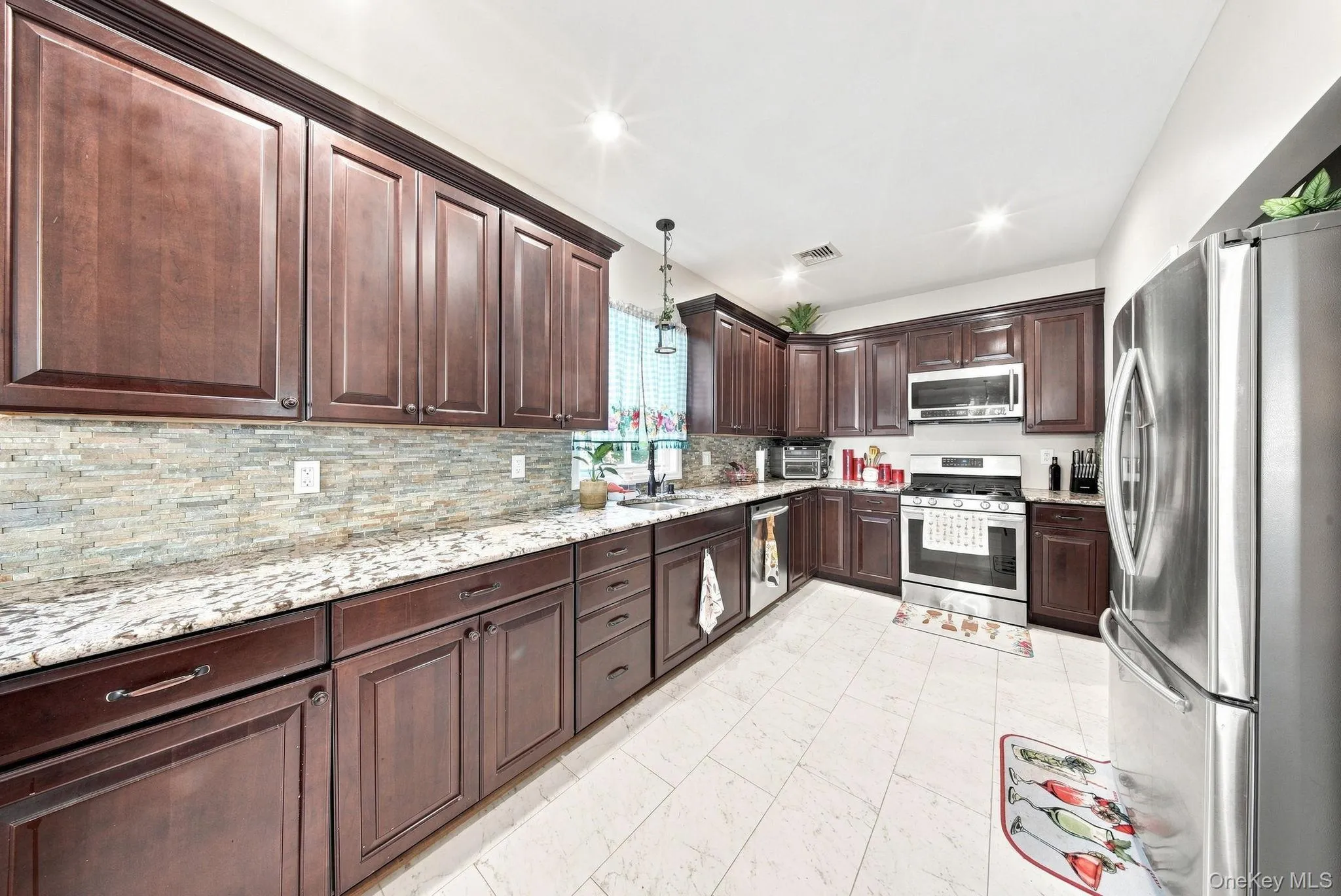Elegant kitchen featuring rich wood cabinetry, stainless steel appliances including a built-in wall oven and refrigerator, granite countertops, and a decorative tile backsplash Elegant kitchen featuring rich wood cabinetry, stainless steel appliances including a built-in wall oven and refrigerator, granite countertops, and a decorative tile backsplash