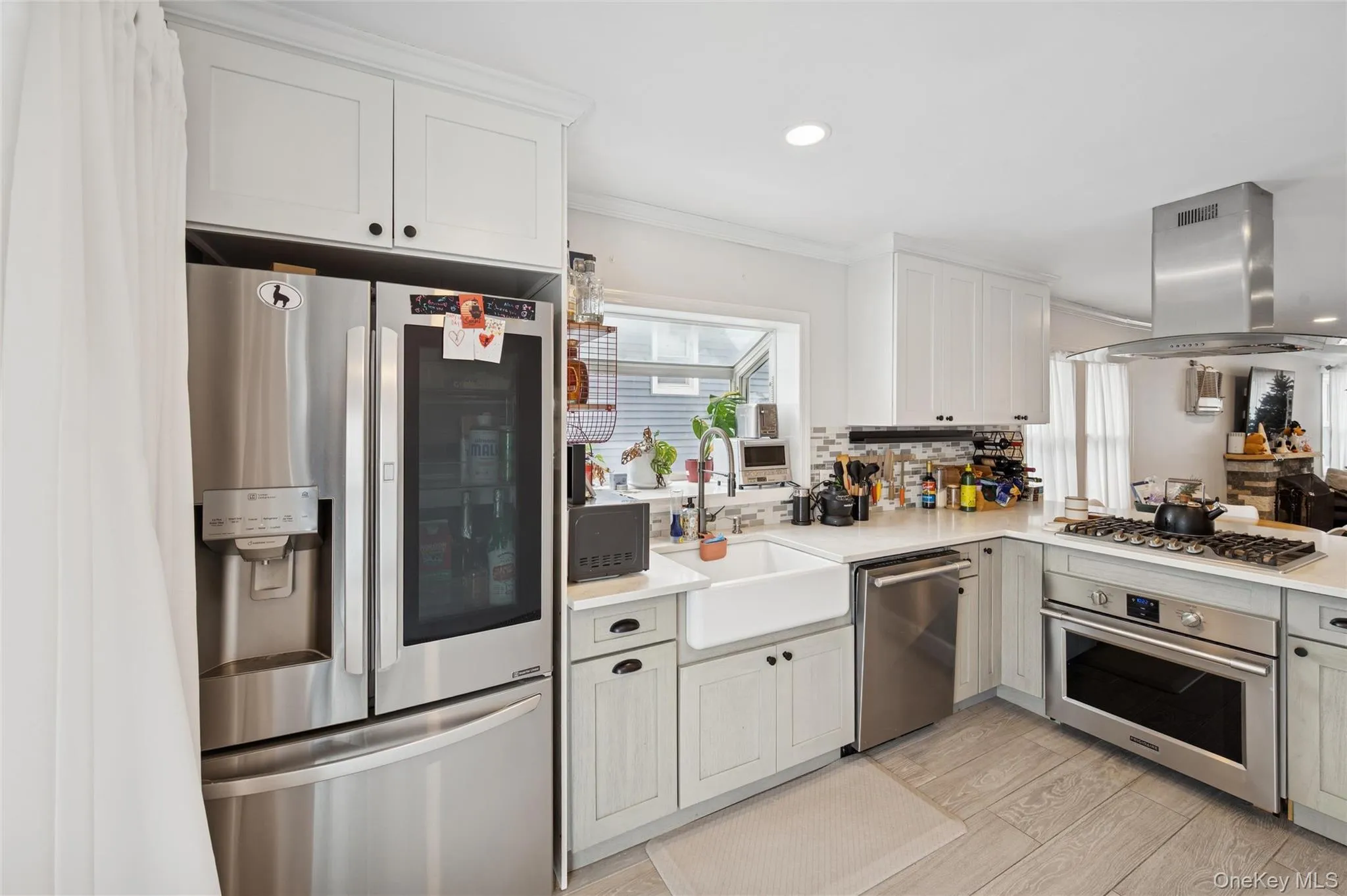 Kitchen with appliances with stainless steel finishes, ornamental molding, island exhaust hood, light wood-style floors, and white cabinets Kitchen with appliances with stainless steel finishes, ornamental molding, island exhaust hood, light wood-style floors, and white cabinets