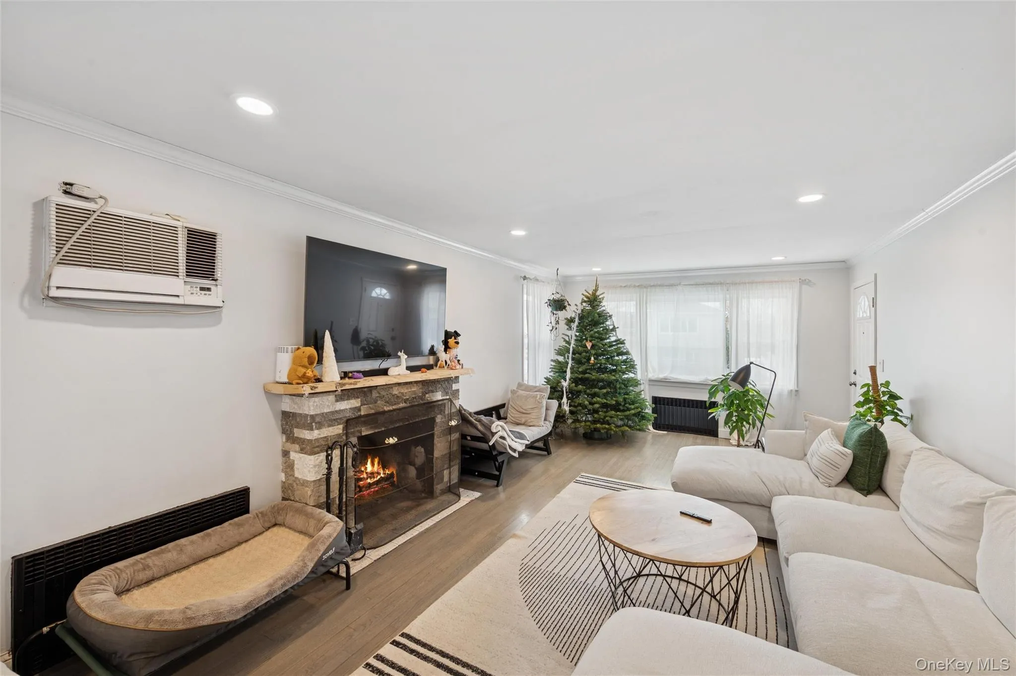 Living area featuring a fireplace, ornamental molding, wood finished floors, a wall mounted air conditioner, and recessed lighting Living area featuring a fireplace, ornamental molding, wood finished floors, a wall mounted air conditioner, and recessed lighting