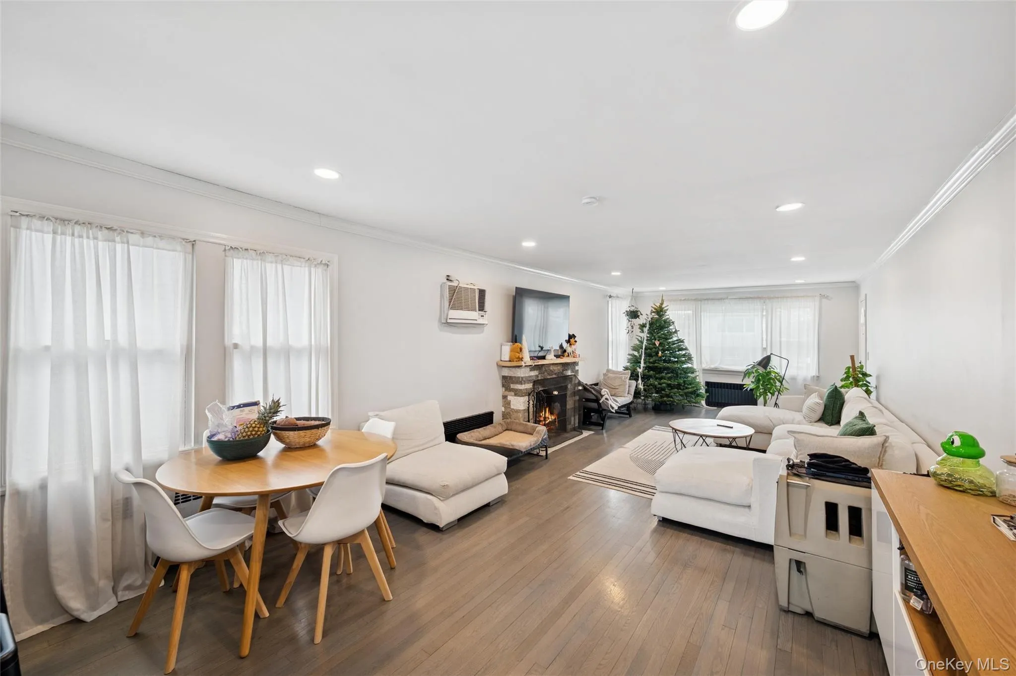 Living area with ornamental molding, dark wood-style floors, a stone fireplace, recessed lighting, and a wall mounted AC Living area with ornamental molding, dark wood-style floors, a stone fireplace, recessed lighting, and a wall mounted AC