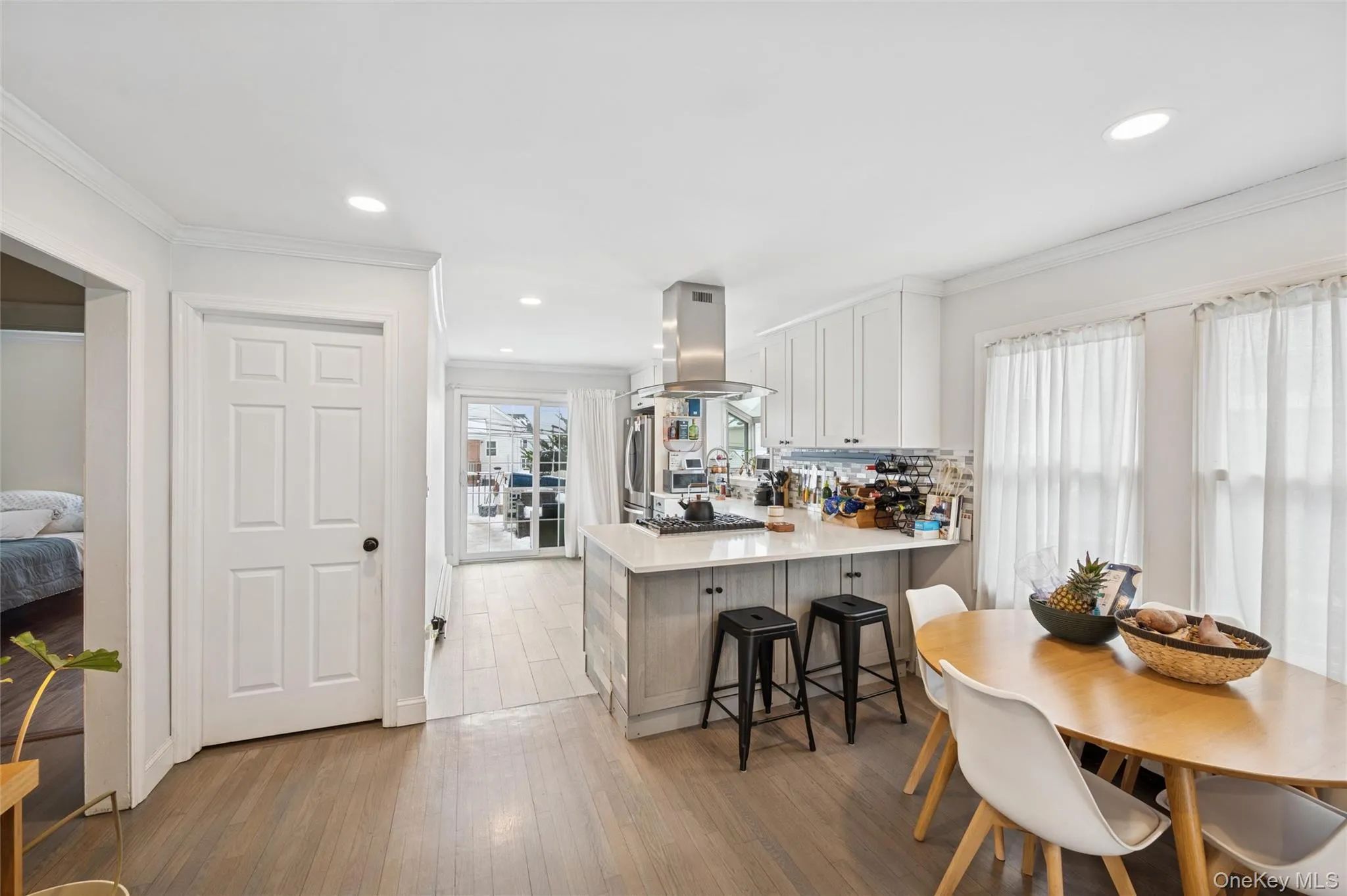 Kitchen featuring crown molding, light wood finished floors, a peninsula, white cabinets, and island range hood Kitchen featuring crown molding, light wood finished floors, a peninsula, white cabinets, and island range hood