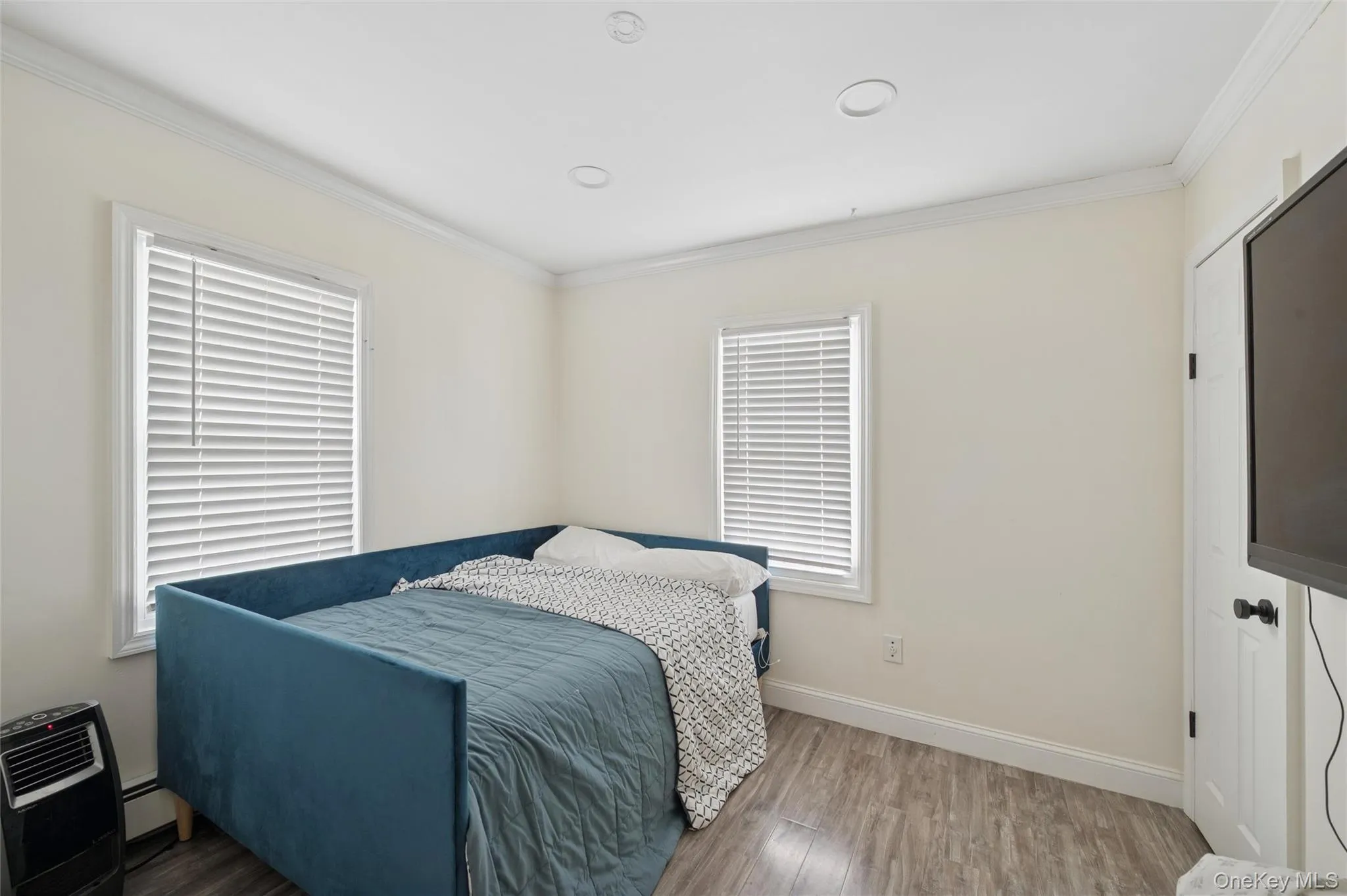 Bedroom with wood finished floors, ornamental molding, and a baseboard heating unit Bedroom with wood finished floors, ornamental molding, and a baseboard heating unit
