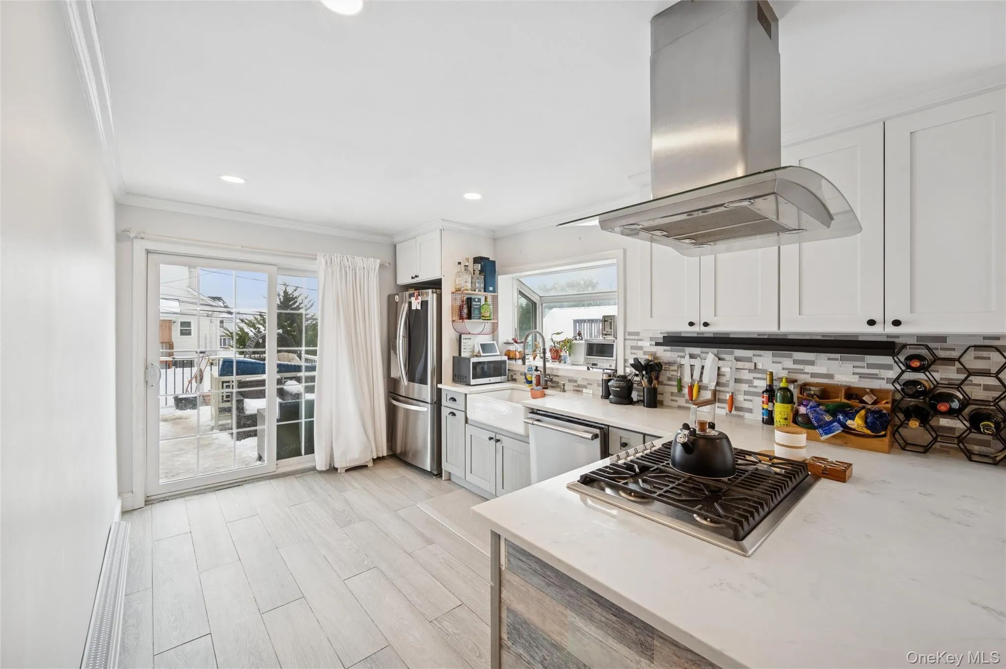 Kitchen featuring island range hood, light stone counters, appliances with stainless steel finishes, ornamental molding, and plenty of natural light Kitchen featuring island range hood, light stone counters, appliances with stainless steel finishes, ornamental molding, and plenty of natural light