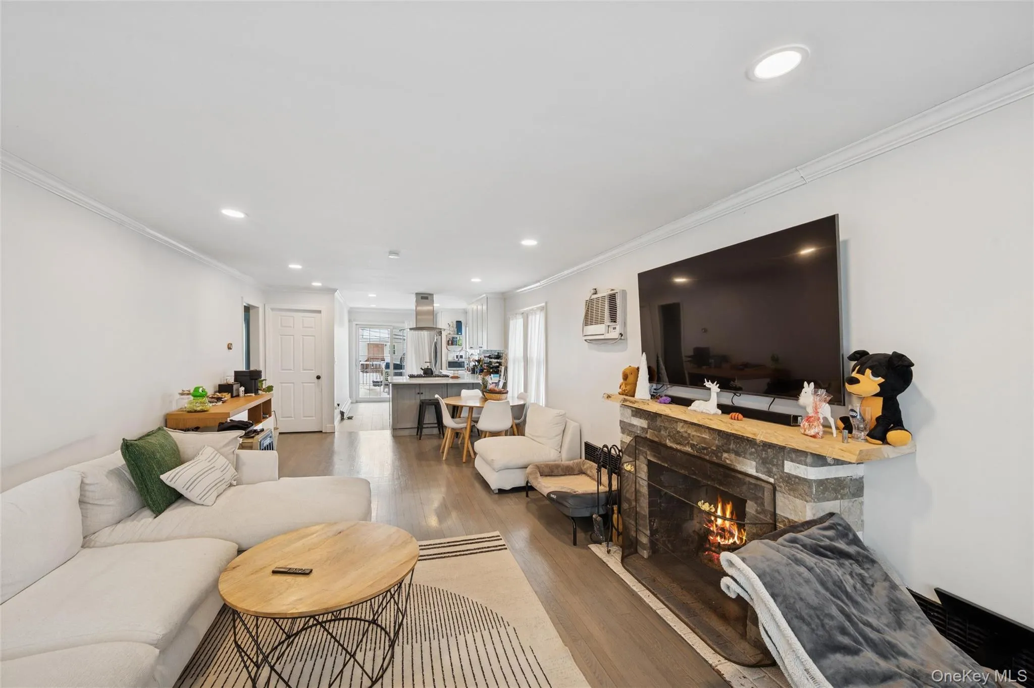 Living area featuring crown molding, a stone fireplace, wood finished floors, and recessed lighting Living area featuring crown molding, a stone fireplace, wood finished floors, and recessed lighting