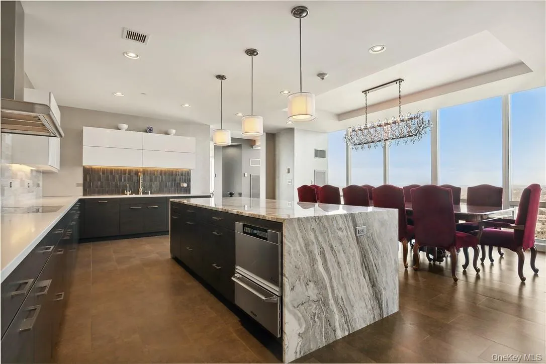 Kitchen featuring decorative light fixtures, wall chimney exhaust hood, white cabinetry, a center island, and light stone countertops Kitchen featuring decorative light fixtures, wall chimney exhaust hood, white cabinetry, a center island, and light stone countertops