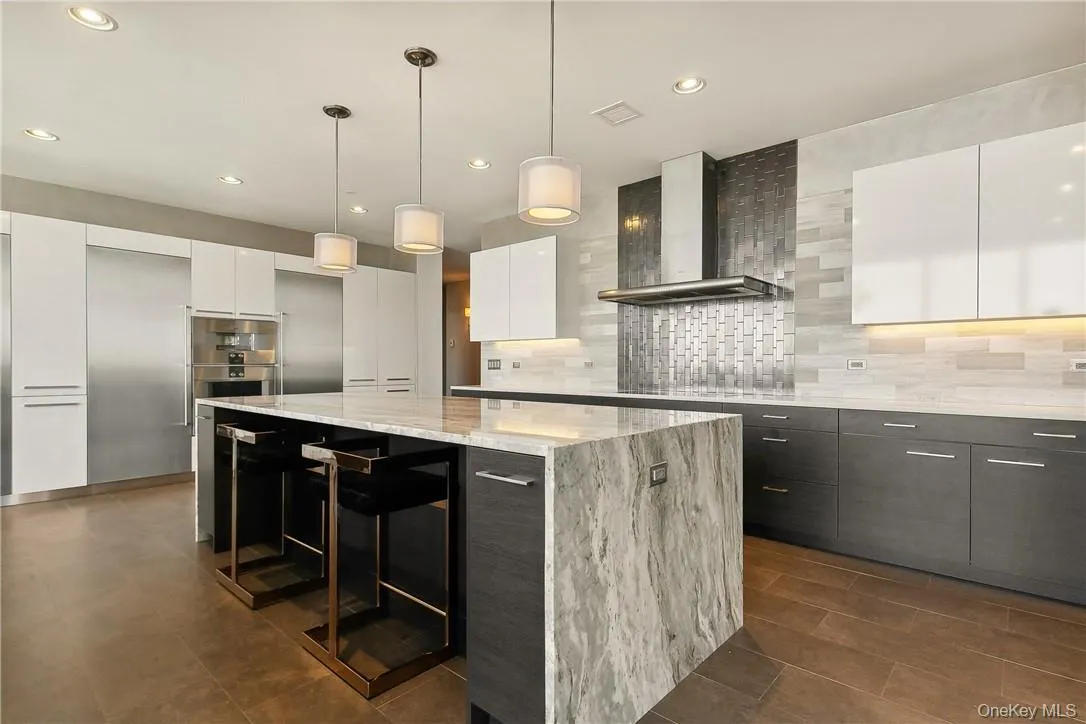Kitchen with decorative backsplash, white cabinets, pendant lighting, a center island, and wall chimney range hood Kitchen with decorative backsplash, white cabinets, pendant lighting, a center island, and wall chimney range hood