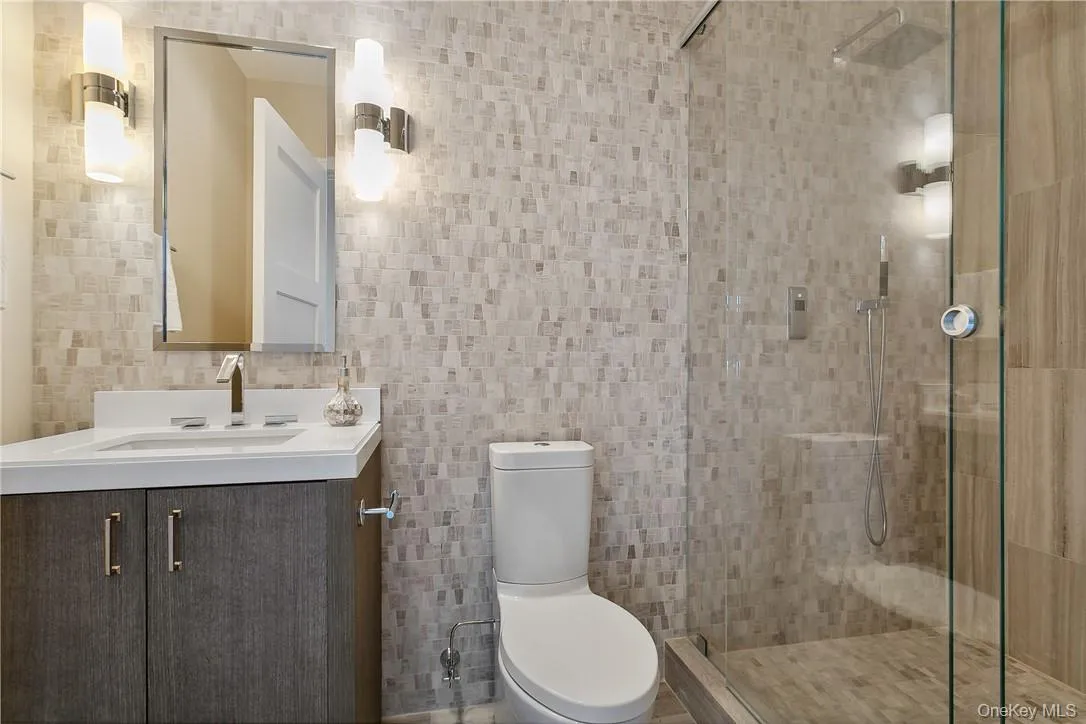 Bathroom featuring tile walls, vanity, toilet, and a shower with door Bathroom featuring tile walls, vanity, toilet, and a shower with door