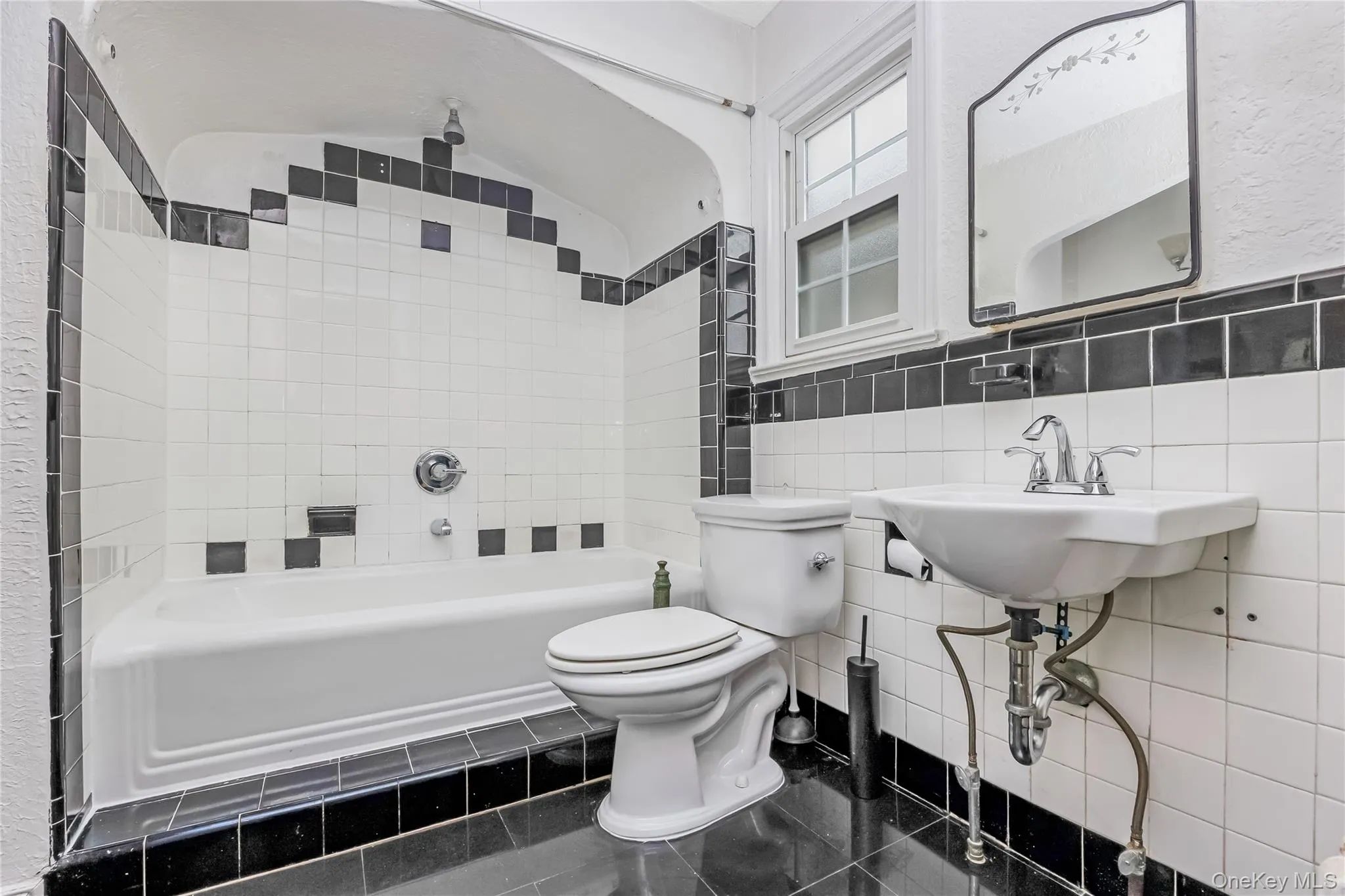 Bathroom with full bathtub, wall-mounted sink, and a black and white tile design Bathroom with full bathtub, wall-mounted sink, and a black and white tile design