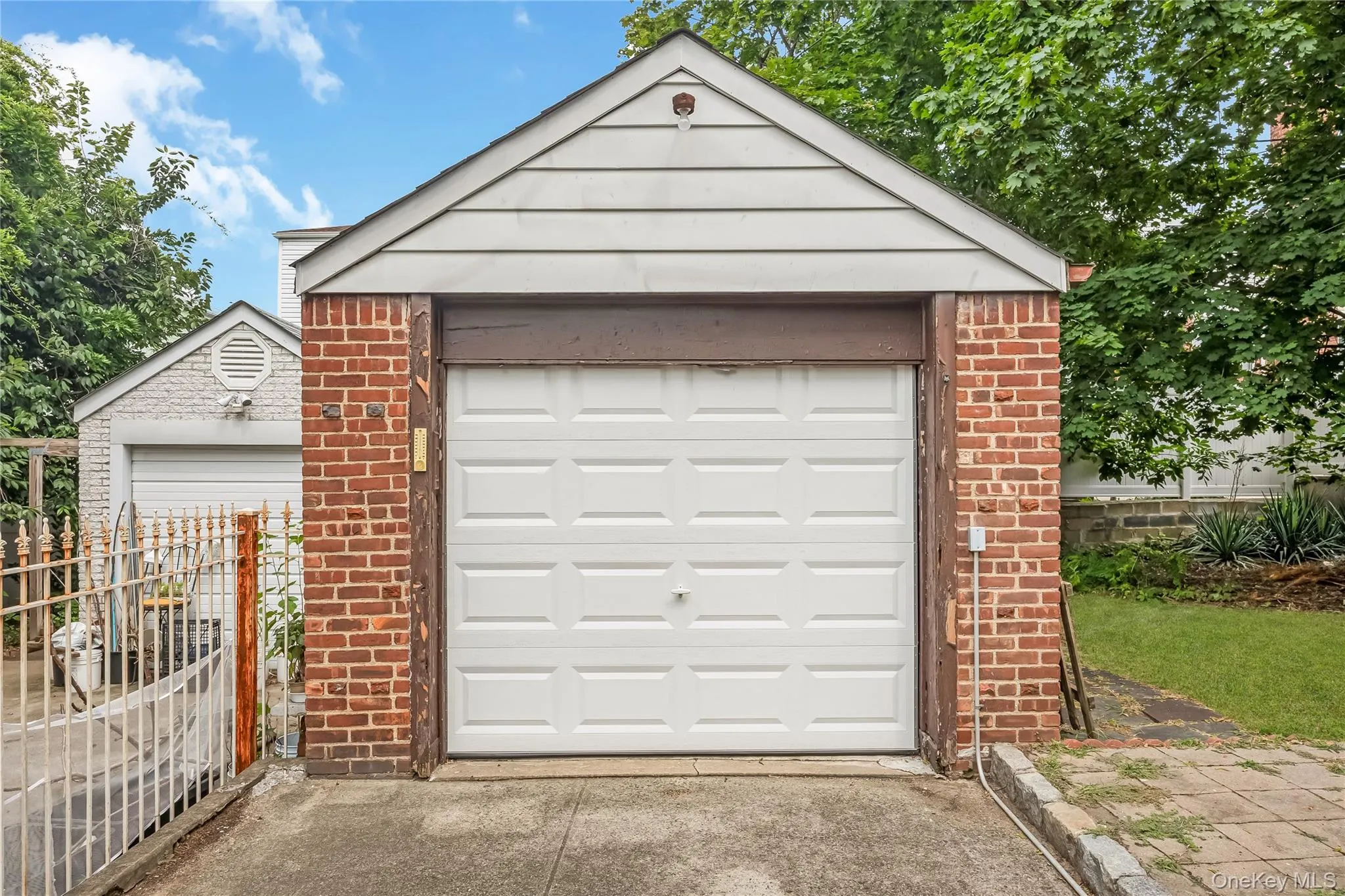 Brick garage featuring a white panel garage door and white siding gable Brick garage featuring a white panel garage door and white siding gable