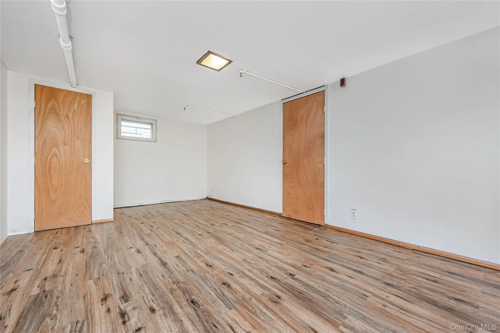 Spacious room featuring wood-finish flooring, white walls, and a recessed ceiling light Spacious room featuring wood-finish flooring, white walls, and a recessed ceiling light