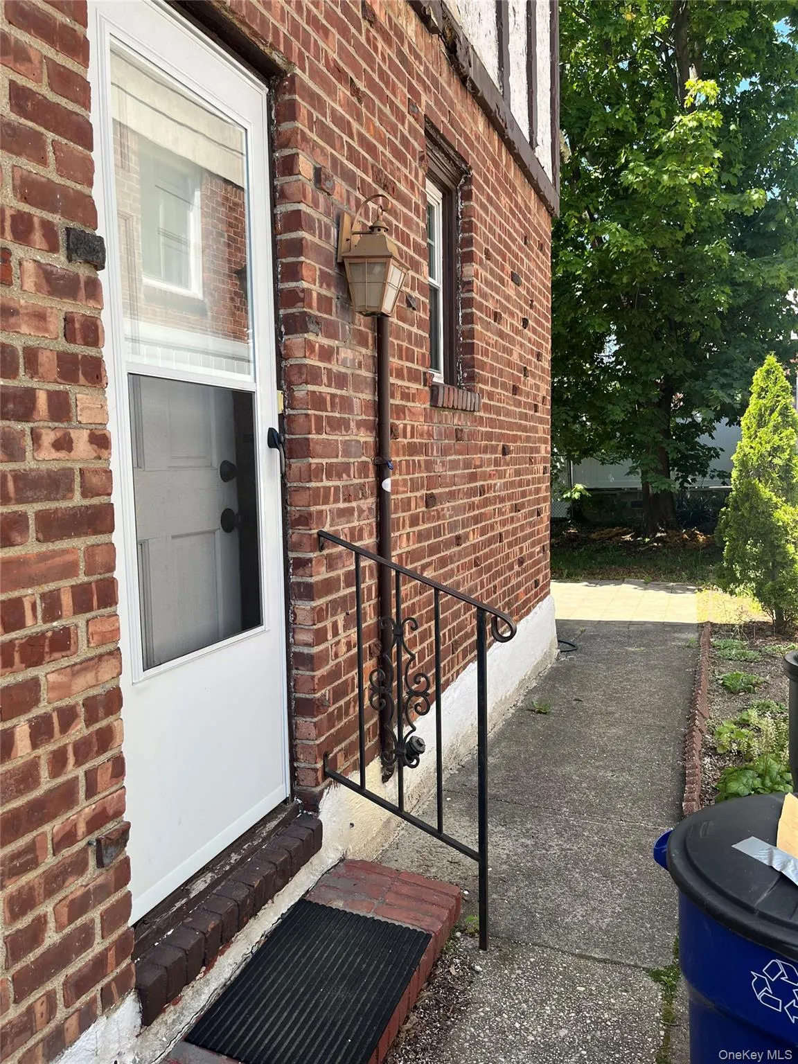 Brick exterior featuring a white storm door, decorative wrought iron handrail, and an exterior wall lantern Brick exterior featuring a white storm door, decorative wrought iron handrail, and an exterior wall lantern