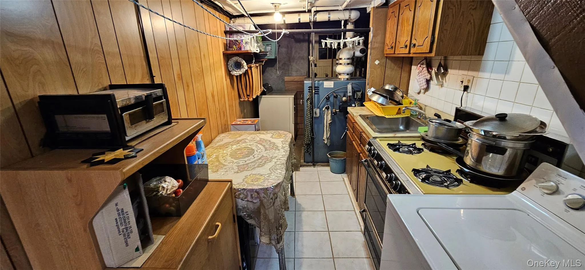 Kitchen featuring washer / dryer, light tile patterned flooring, brown cabinetry, a heating unit, and light countertops Kitchen featuring washer / dryer, light tile patterned flooring, brown cabinetry, a heating unit, and light countertops