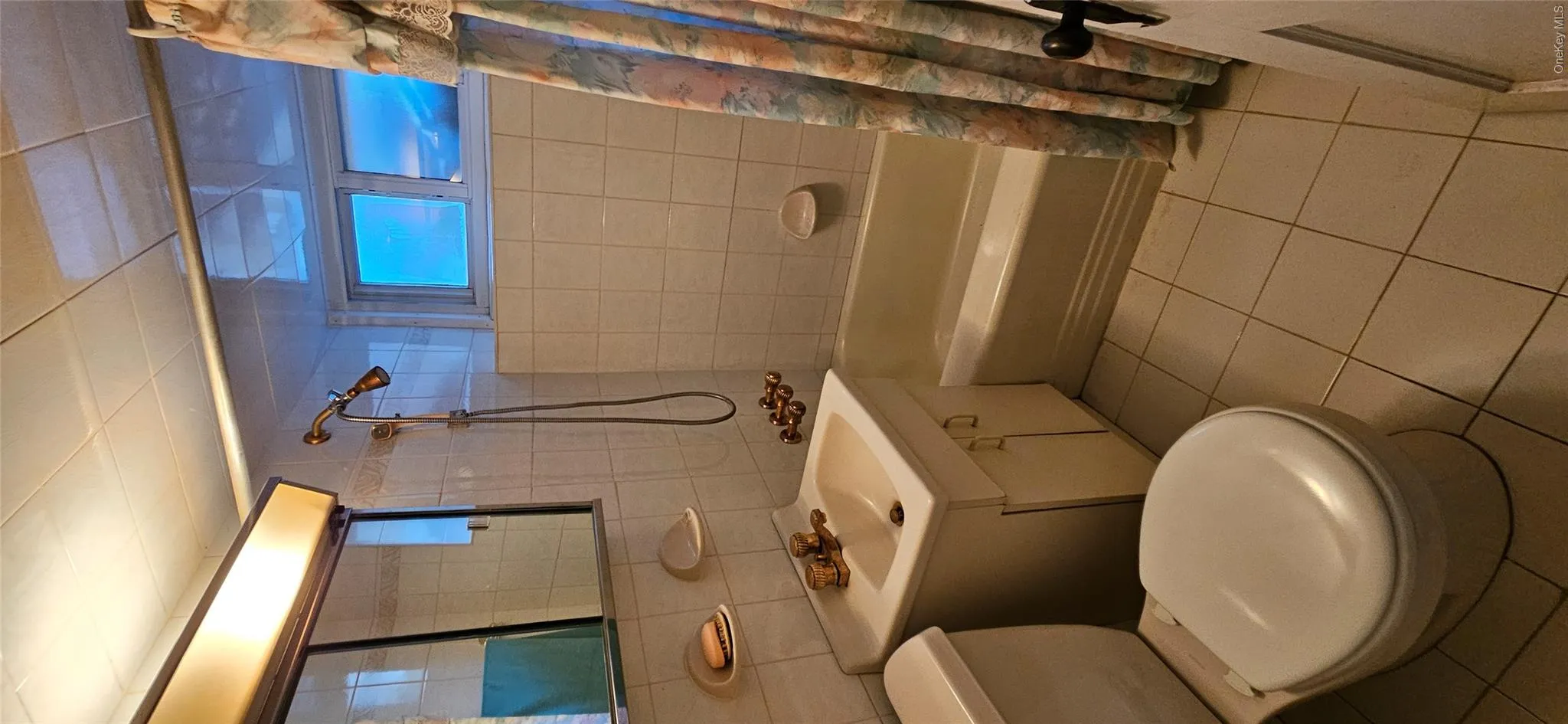 Full bath featuring light tile patterned floors, shower / tub combo, vanity, and tile walls Full bath featuring light tile patterned floors, shower / tub combo, vanity, and tile walls
