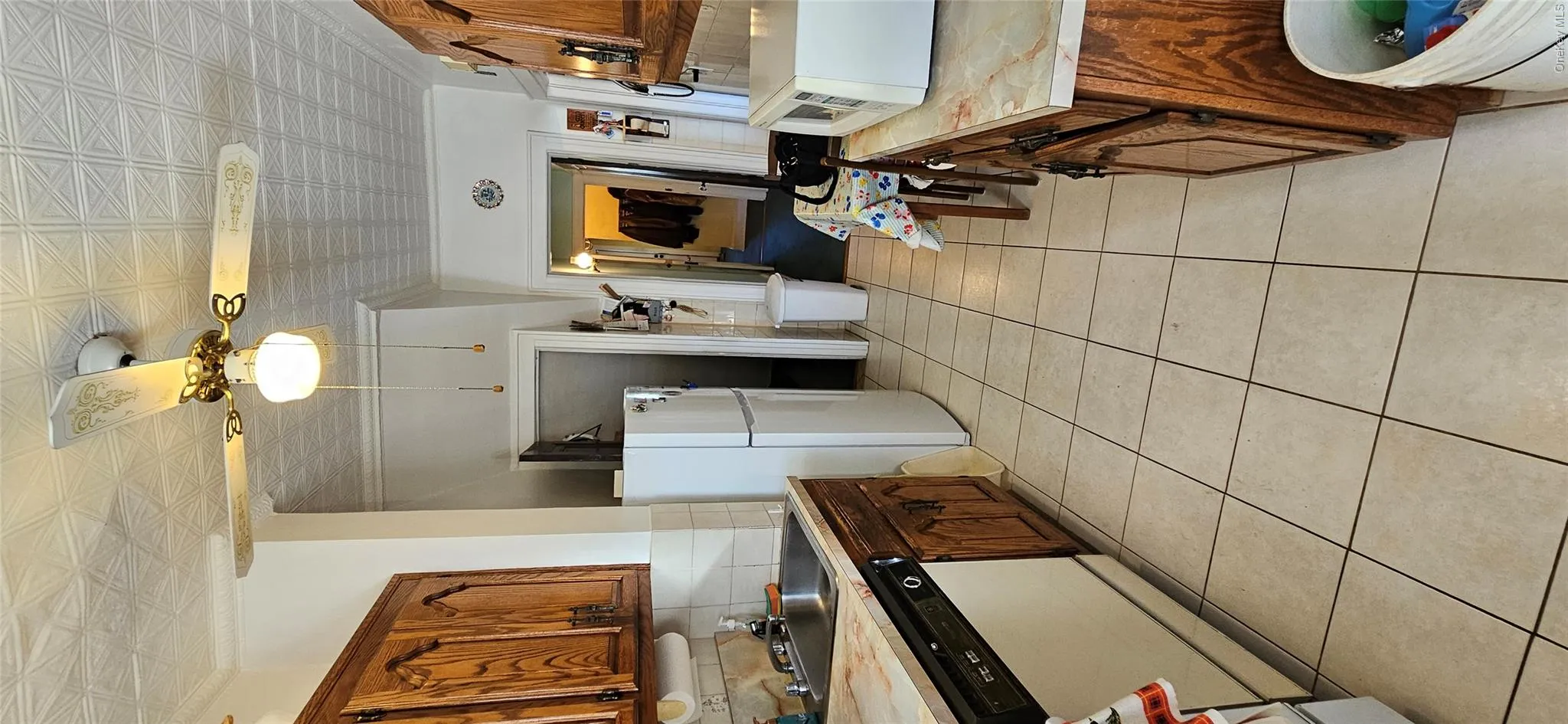 Kitchen with light countertops, backsplash, brown cabinetry, dishwasher, and white refrigerator Kitchen with light countertops, backsplash, brown cabinetry, dishwasher, and white refrigerator