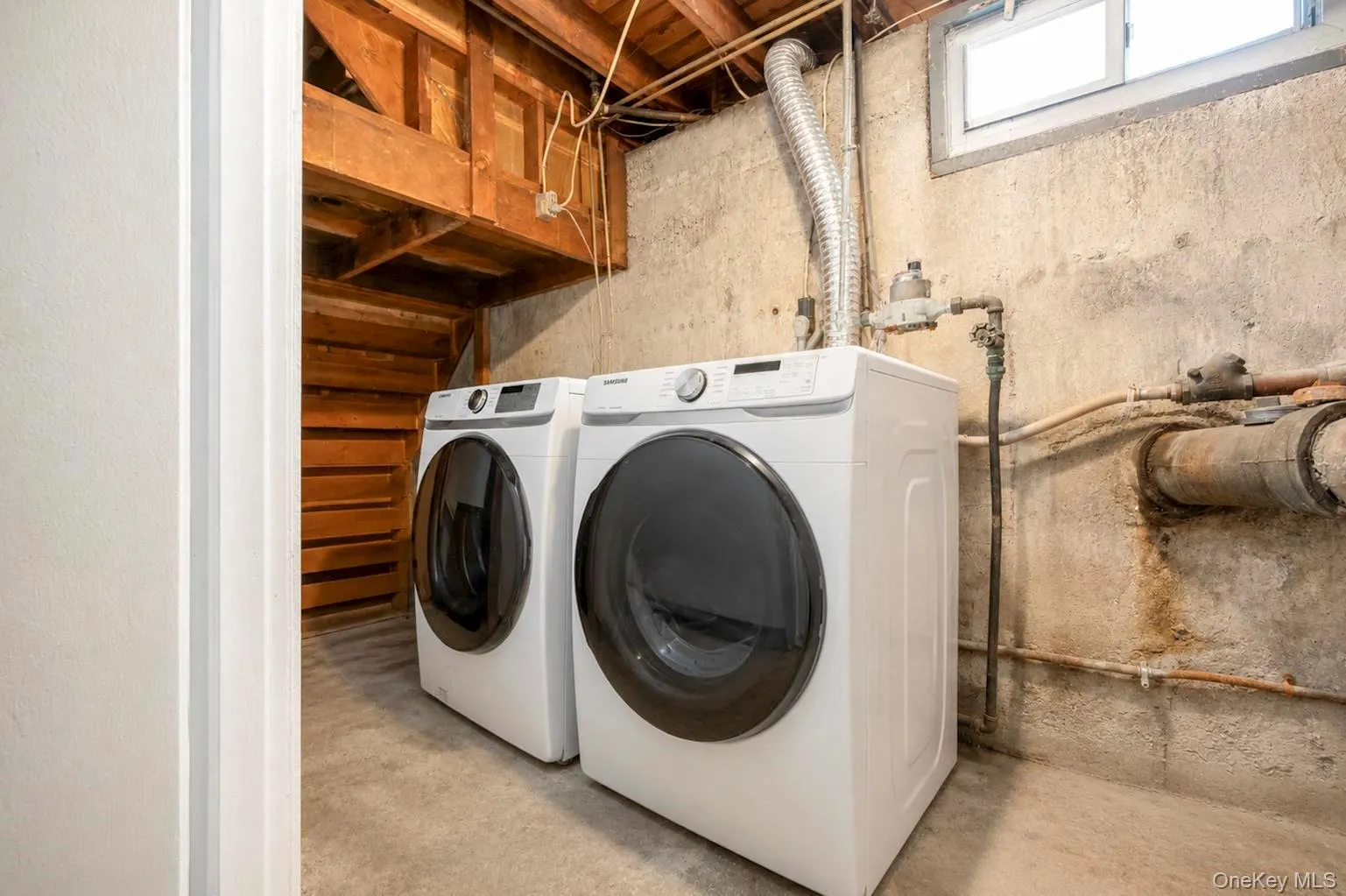 Laundry area featuring a concrete floor, exposed wooden ceiling joists, and a sliding window Laundry area featuring a concrete floor, exposed wooden ceiling joists, and a sliding window