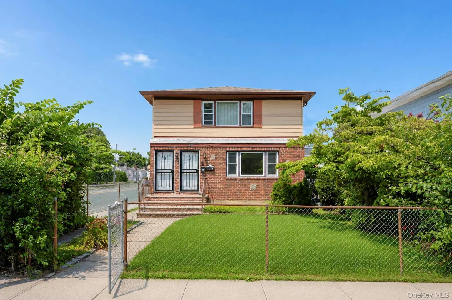 Two-story property featuring a brick lower level and horizontal siding on the upper level, surrounded by mature perimeter foliage Two-story property featuring a brick lower level and horizontal siding on the upper level, surrounded by mature perimeter foliage