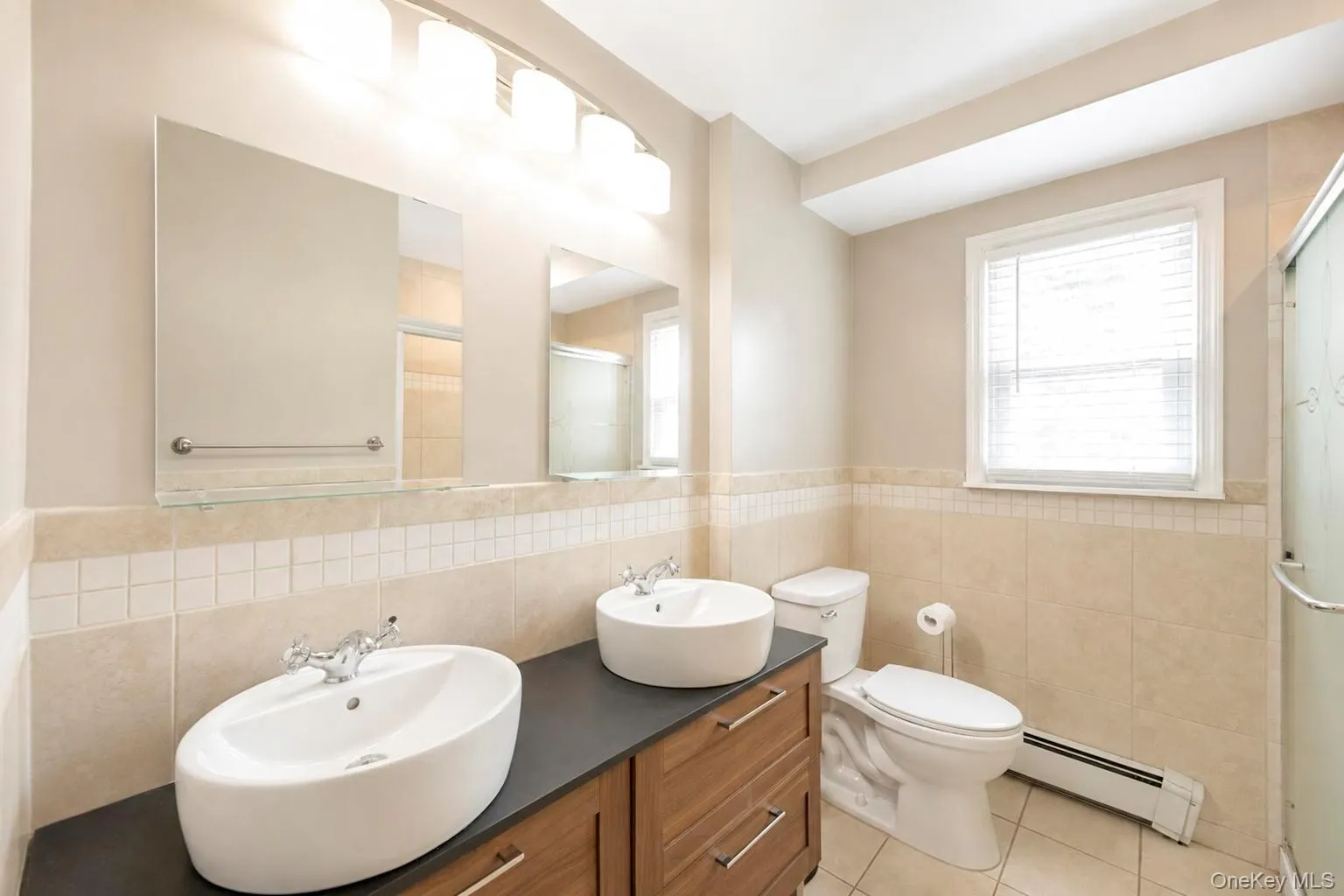 Bathroom featuring a dual vanity with vessel sinks, a brown wood-finish cabinet, and a dark countertop Bathroom featuring a dual vanity with vessel sinks, a brown wood-finish cabinet, and a dark countertop