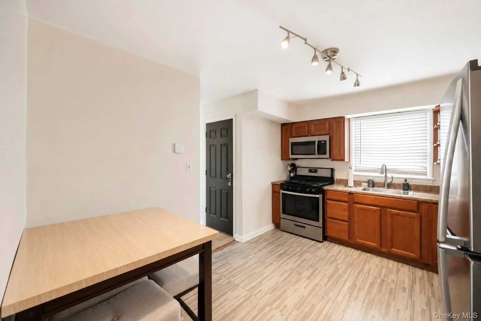 Kitchen featuring wood-finish flooring, stainless steel appliances, wood cabinetry, stone countertops, and a track lighting fixture Kitchen featuring wood-finish flooring, stainless steel appliances, wood cabinetry, stone countertops, and a track lighting fixture