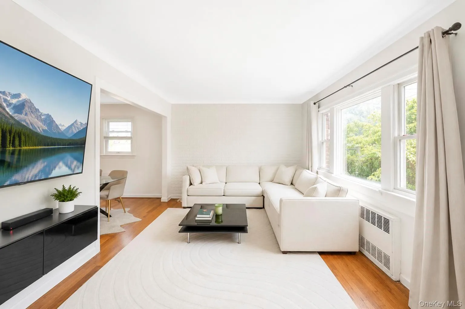 Living area featuring hardwood flooring, extensive natural light, an open doorway, and a ceiling-mounted wall heater Living area featuring hardwood flooring, extensive natural light, an open doorway, and a ceiling-mounted wall heater