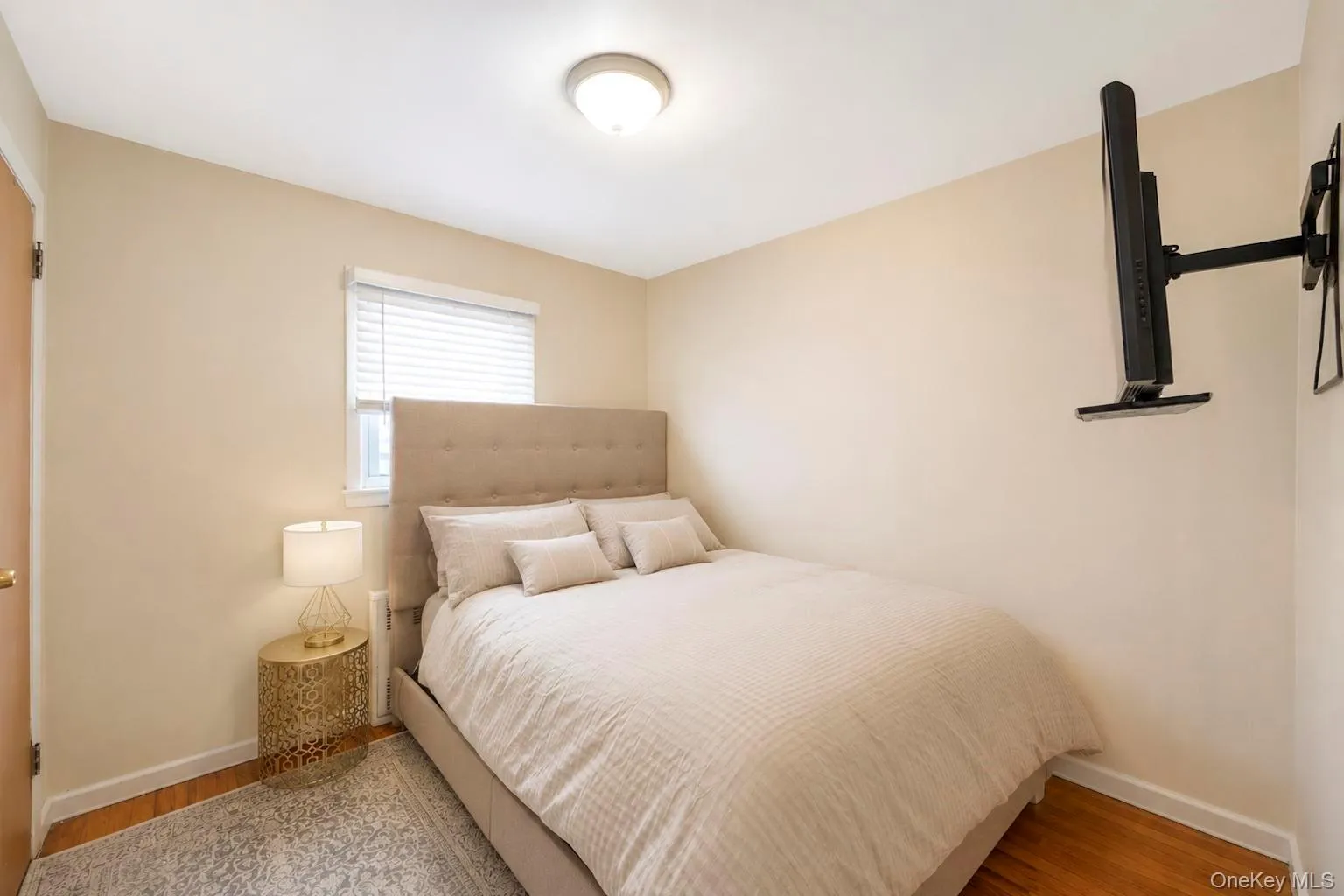 Bedroom featuring neutral wall color, hardwood flooring, a single window with blinds, and a ceiling-mounted light fixture Bedroom featuring neutral wall color, hardwood flooring, a single window with blinds, and a ceiling-mounted light fixture