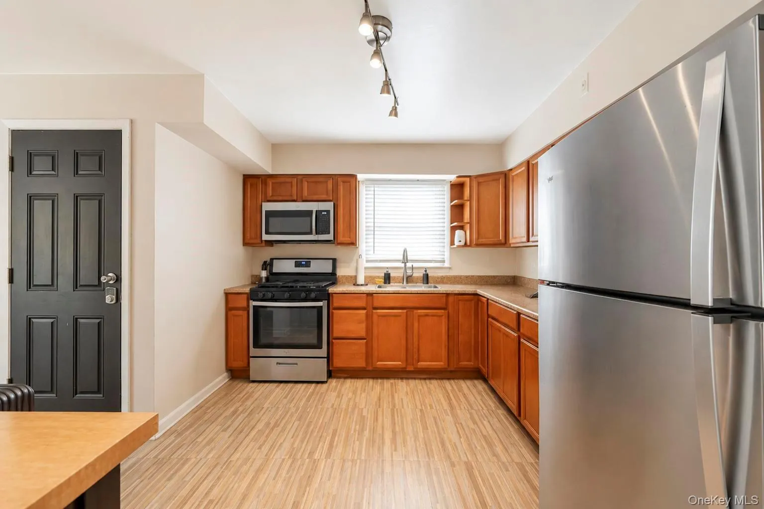 Kitchen featuring wood-finish flooring, stainless steel appliances, wood cabinetry, light-toned countertops, and track lighting Kitchen featuring wood-finish flooring, stainless steel appliances, wood cabinetry, light-toned countertops, and track lighting