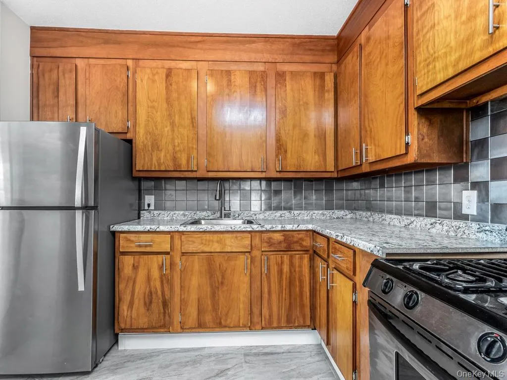 Kitchen featuring wood-finish cabinetry with silver-tone hardware, a stainless steel refrigerator, and a stainless steel range Kitchen featuring wood-finish cabinetry with silver-tone hardware, a stainless steel refrigerator, and a stainless steel range
