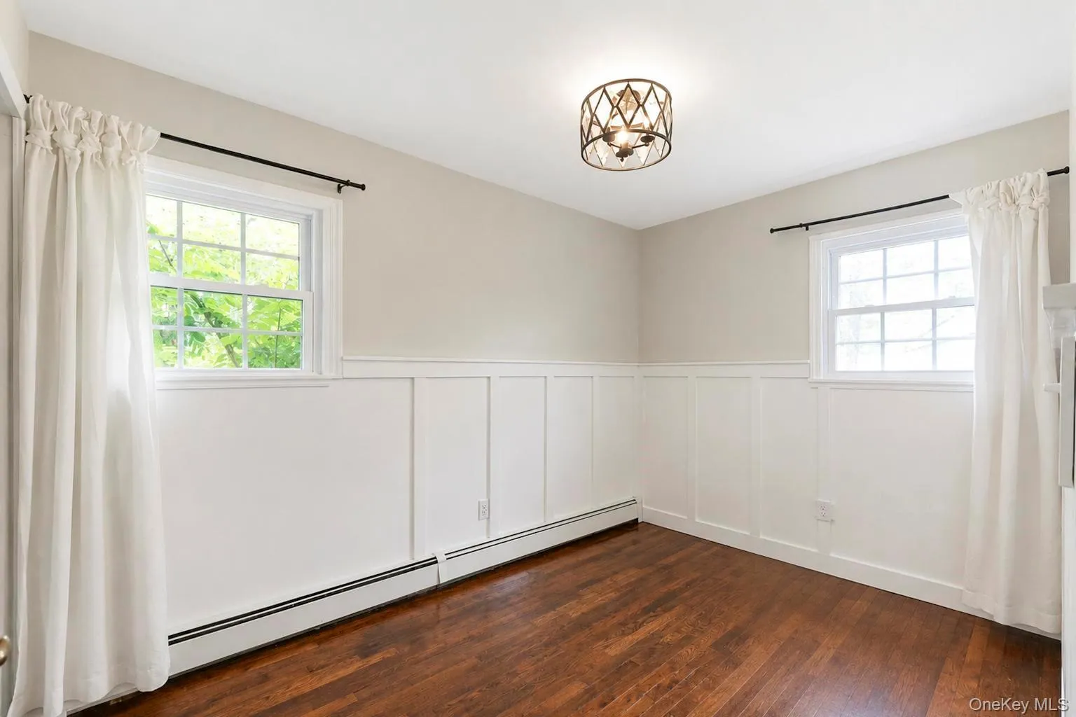 Bedroom #2 featuring dark wood-finish flooring, white wainscoting, two windows, and a decorative semi-flush mount ceiling fixture Bedroom #2 featuring dark wood-finish flooring, white wainscoting, two windows, and a decorative semi-flush mount ceiling fixture