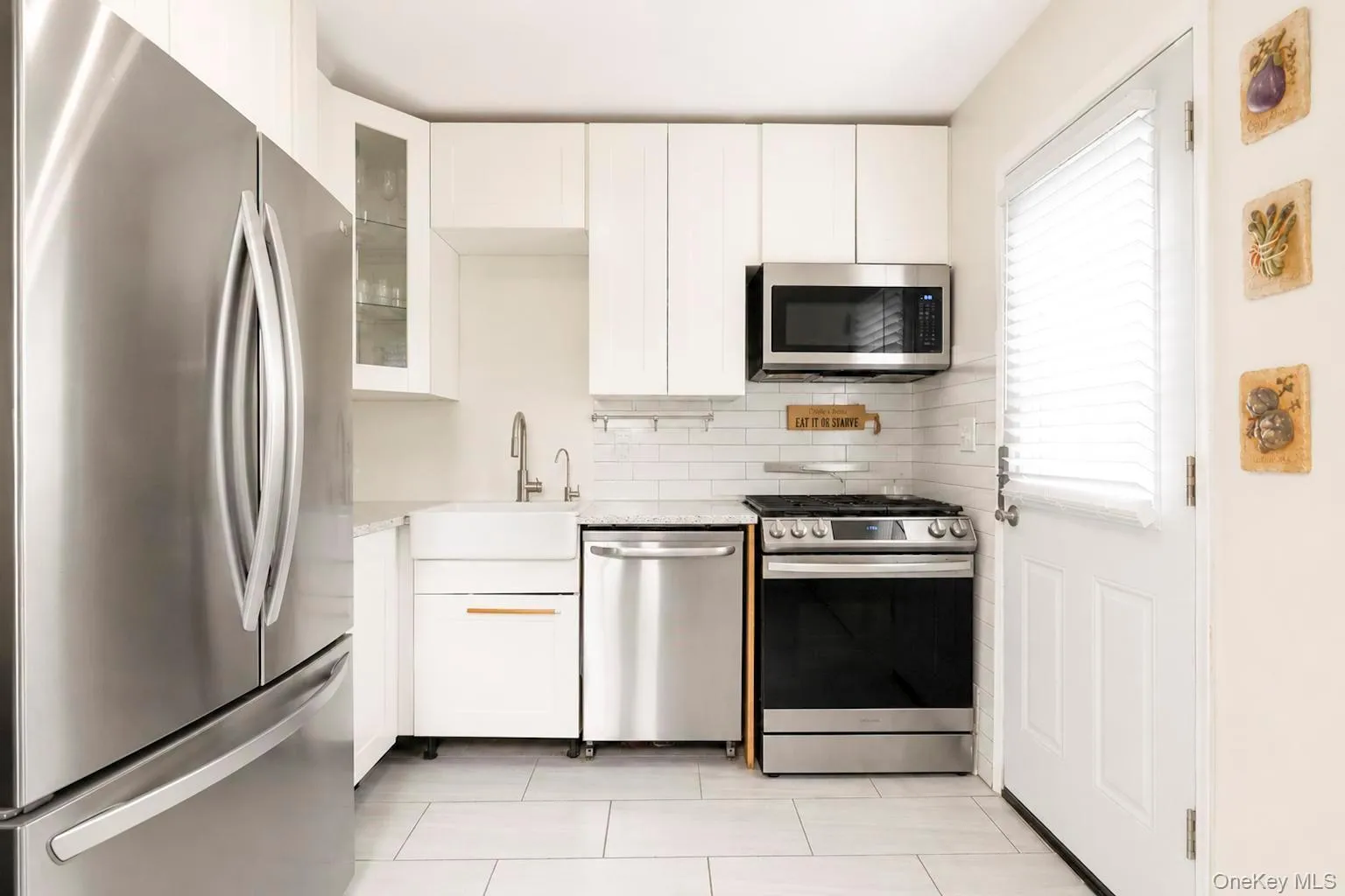 Contemporary kitchen featuring white cabinetry, stainless steel appliances, subway tile backsplash, and light-toned tile flooring Contemporary kitchen featuring white cabinetry, stainless steel appliances, subway tile backsplash, and light-toned tile flooring