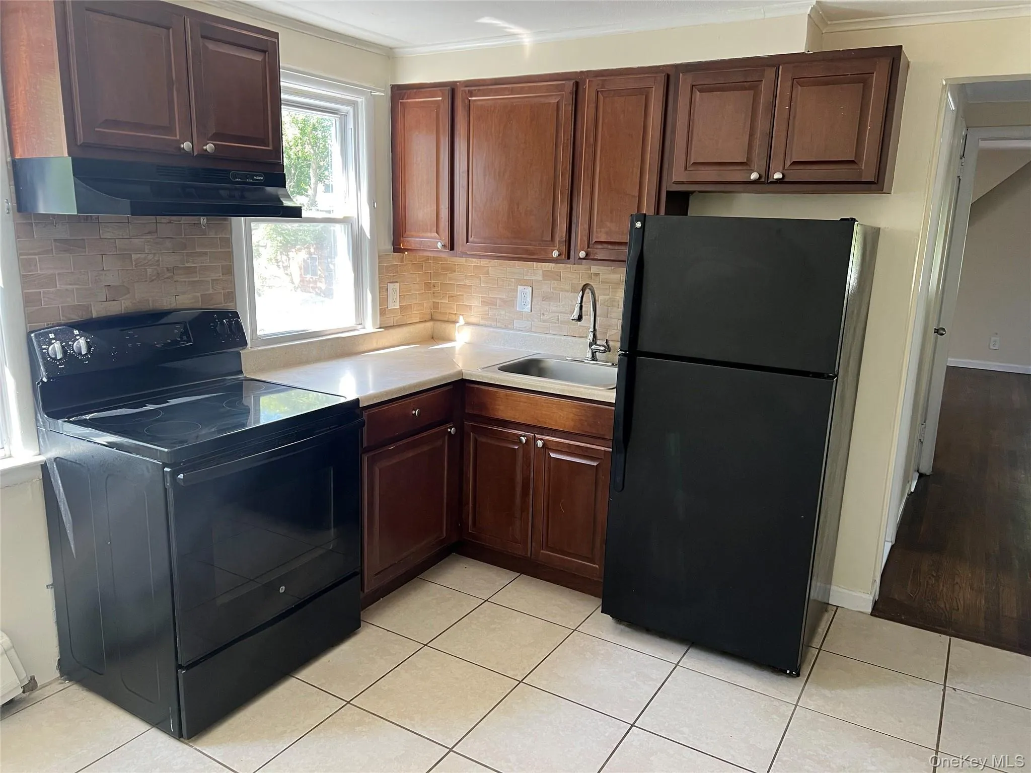 Kitchen with black appliances, light countertops, light tile patterned flooring, under cabinet range hood, and decorative backsplash Kitchen with black appliances, light countertops, light tile patterned flooring, under cabinet range hood, and decorative backsplash
