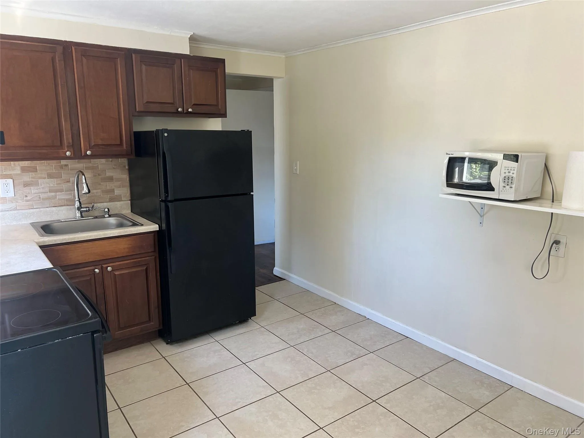 Kitchen with black appliances, light countertops, tasteful backsplash, ornamental molding, and dark brown cabinetry Kitchen with black appliances, light countertops, tasteful backsplash, ornamental molding, and dark brown cabinetry