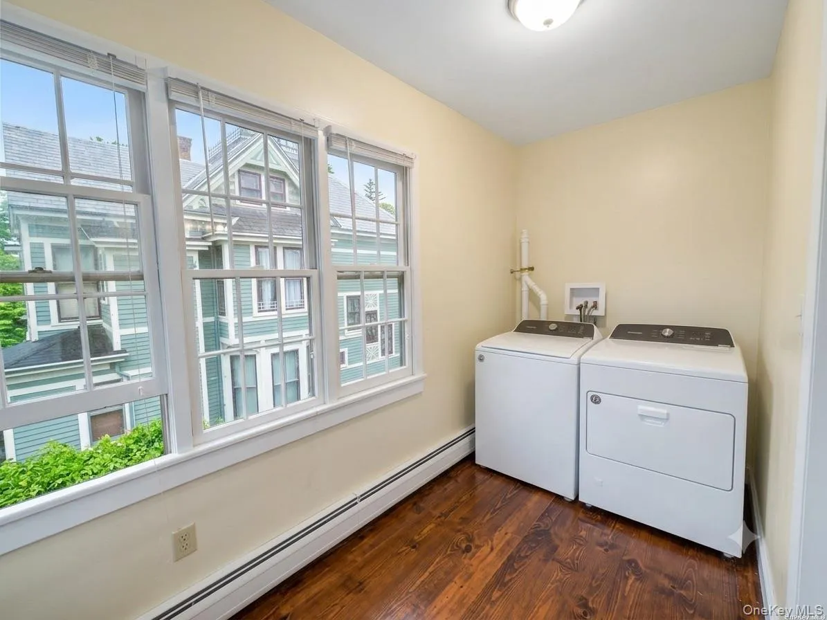 Dedicated laundry area featuring wood-finish flooring, multiple windows, and baseboard heating Dedicated laundry area featuring wood-finish flooring, multiple windows, and baseboard heating