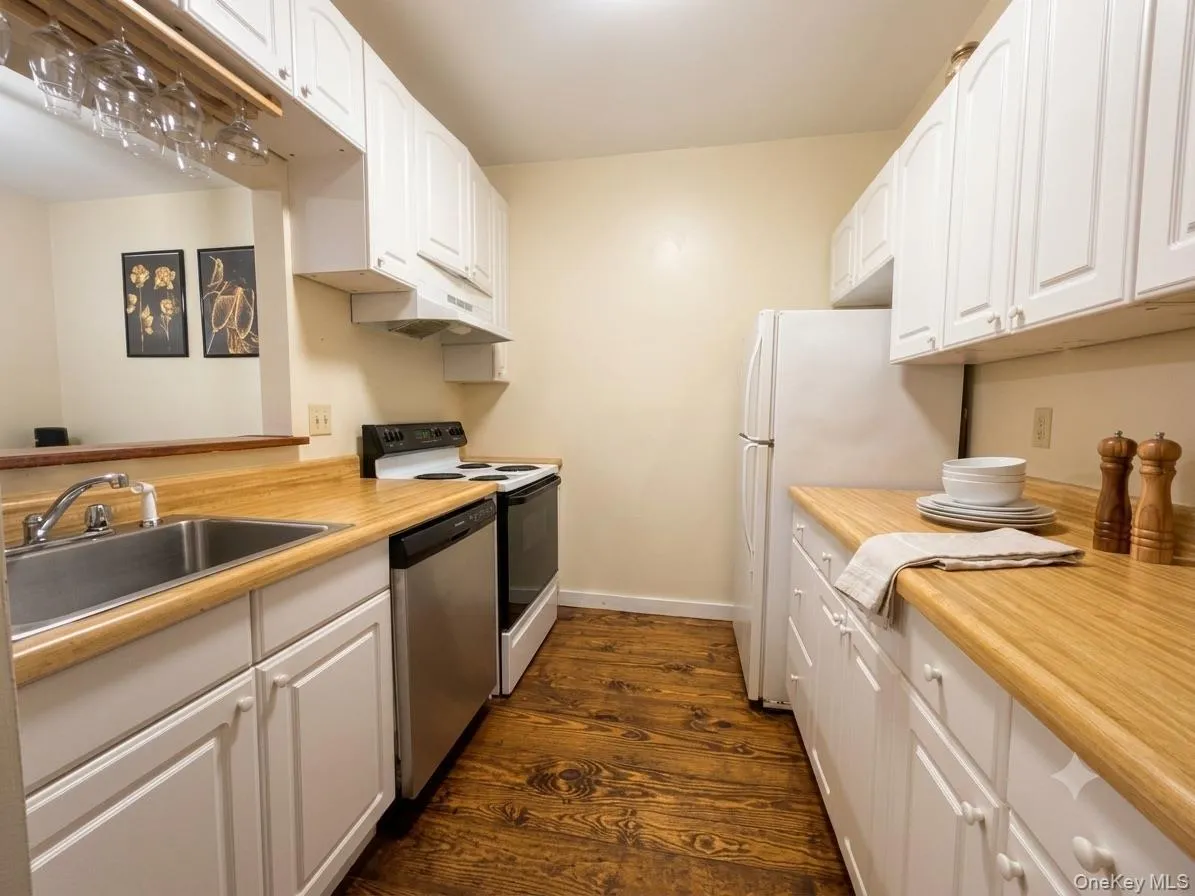 Kitchen featuring wood-finish flooring, white cabinetry, a stainless steel sink, and light wood-tone countertops Kitchen featuring wood-finish flooring, white cabinetry, a stainless steel sink, and light wood-tone countertops
