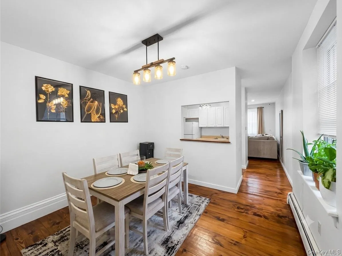 Dining area featuring wood-finish flooring, a contemporary linear chandelier, and a pass-through opening to the kitchen Dining area featuring wood-finish flooring, a contemporary linear chandelier, and a pass-through opening to the kitchen