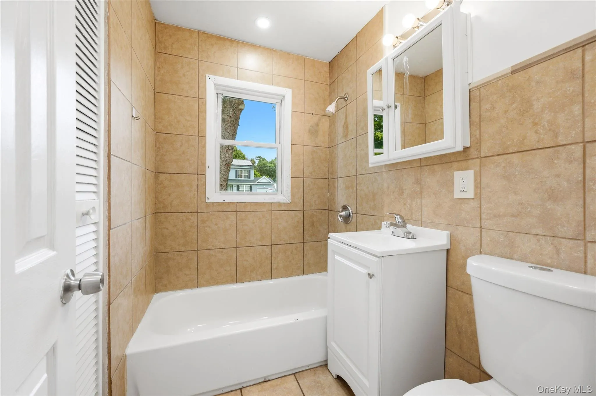 Bathroom featuring floor-to-ceiling tile, single window, white vanity, and built-in medicine cabinet Bathroom featuring floor-to-ceiling tile, single window, white vanity, and built-in medicine cabinet
