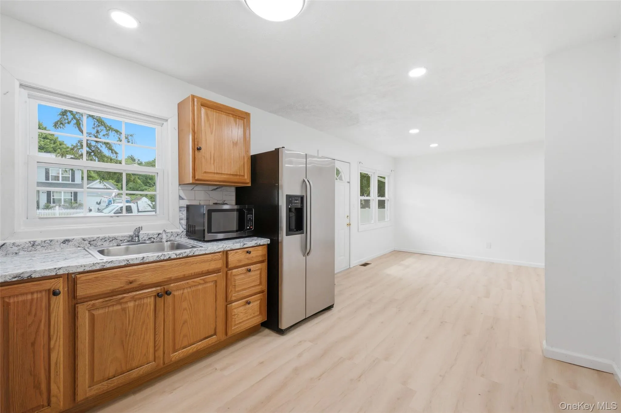 Kitchen area featuring wood cabinetry, white stone-look countertops, and a stainless steel sink Kitchen area featuring wood cabinetry, white stone-look countertops, and a stainless steel sink