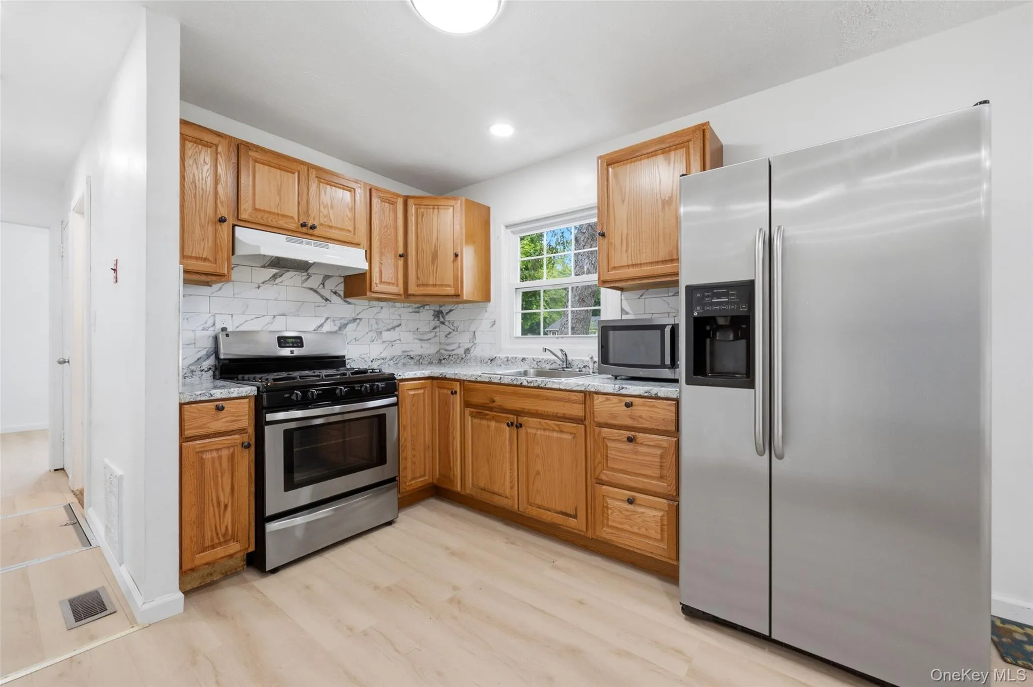 Kitchen featuring wood-finish cabinetry, light-toned countertops, and a white marble-patterned tile backsplash Kitchen featuring wood-finish cabinetry, light-toned countertops, and a white marble-patterned tile backsplash