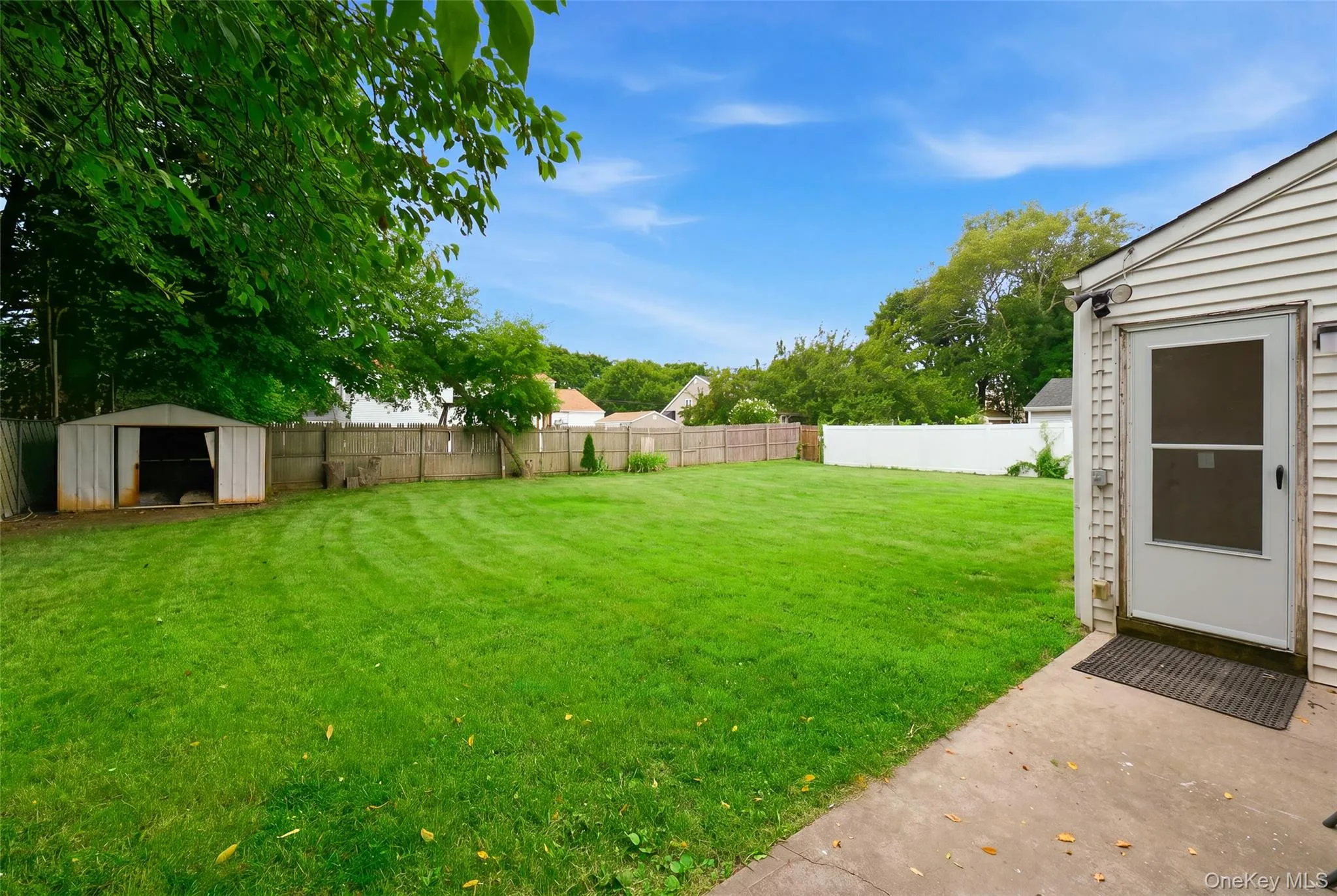 Expansive green lawn with a storage shed, wood fence, and white privacy fence Expansive green lawn with a storage shed, wood fence, and white privacy fence