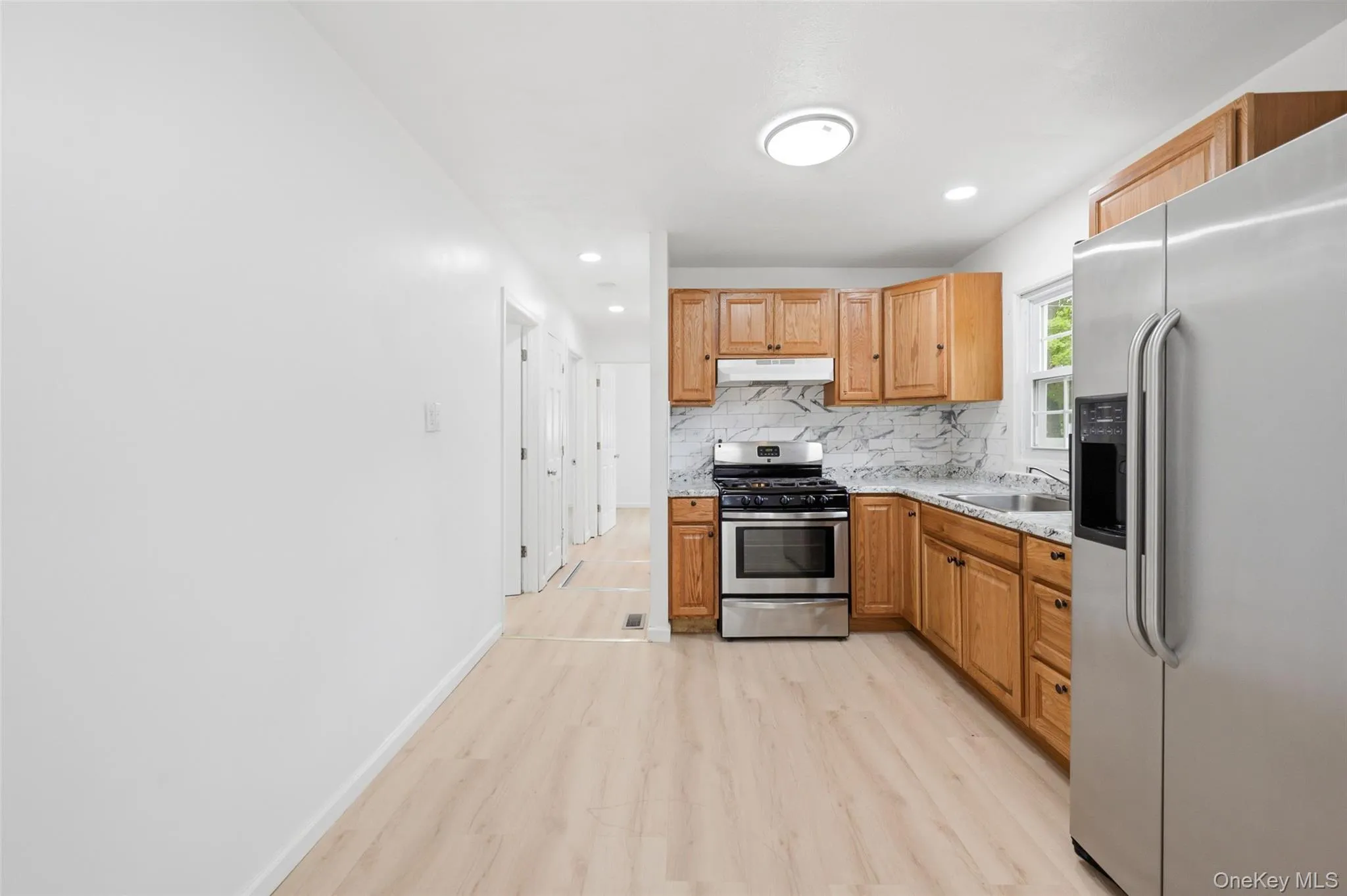 Kitchen featuring wood-finish cabinetry, stainless steel appliances, granite-style countertops, and a white marble-patterned backsplash Kitchen featuring wood-finish cabinetry, stainless steel appliances, granite-style countertops, and a white marble-patterned backsplash