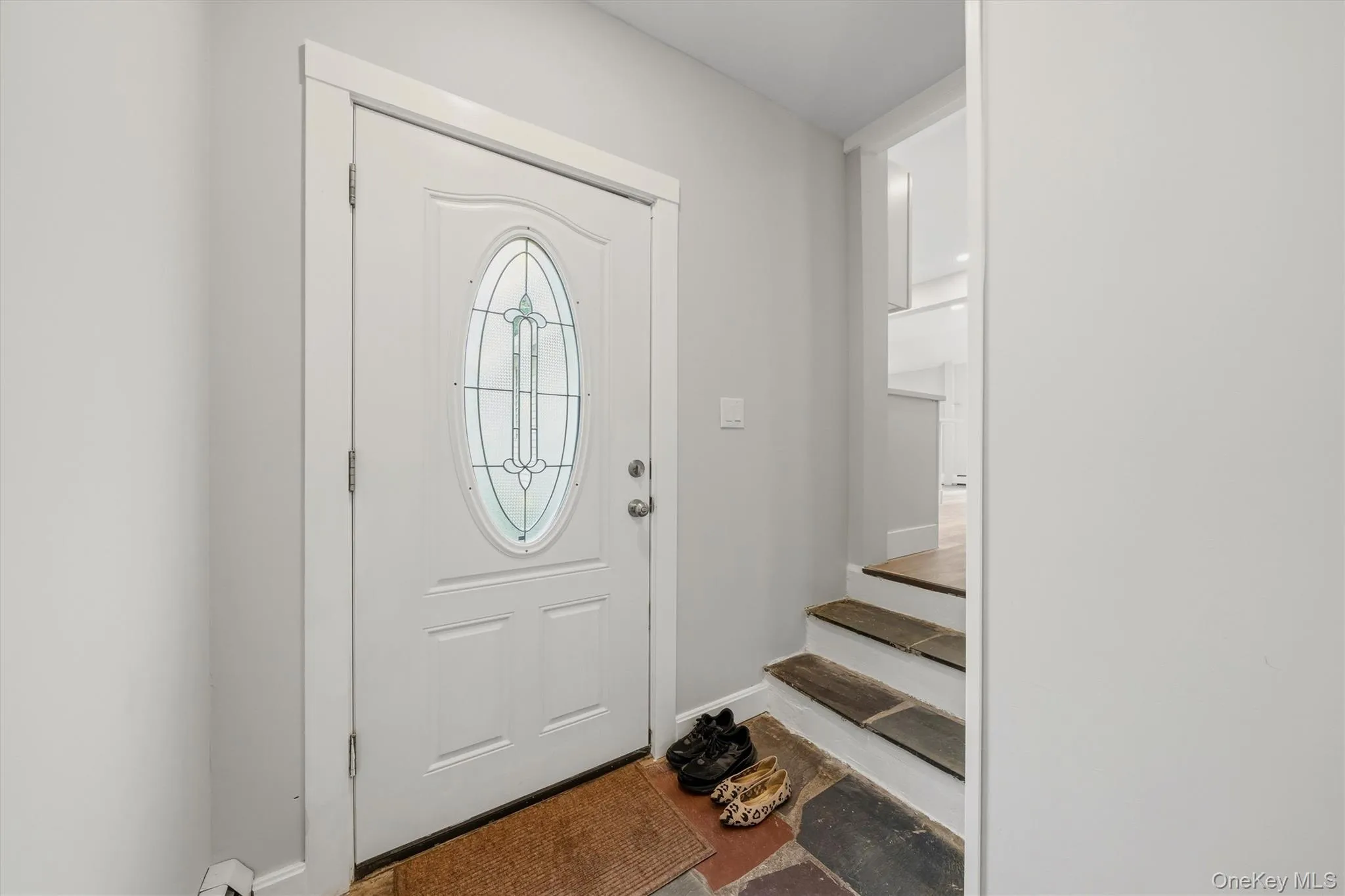 Front entry with a decorative oval glass insert door, white trim, light gray walls, and stone-finish flooring at the base of the stairs Front entry with a decorative oval glass insert door, white trim, light gray walls, and stone-finish flooring at the base of the stairs