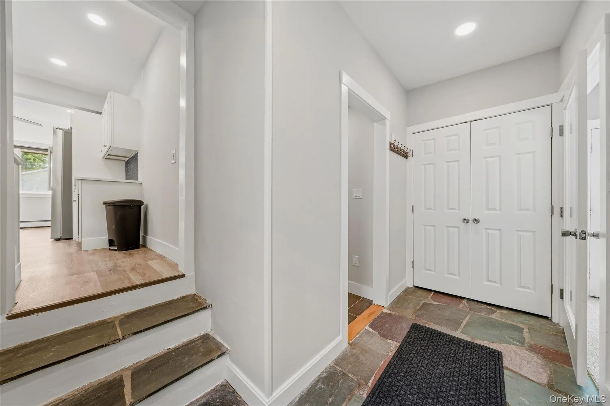 Foyer featuring natural stone tile flooring, recessed lighting, white paneled doors, and access to an additional living space with wood-finish flooring and white cabinetry Foyer featuring natural stone tile flooring, recessed lighting, white paneled doors, and access to an additional living space with wood-finish flooring and white cabinetry