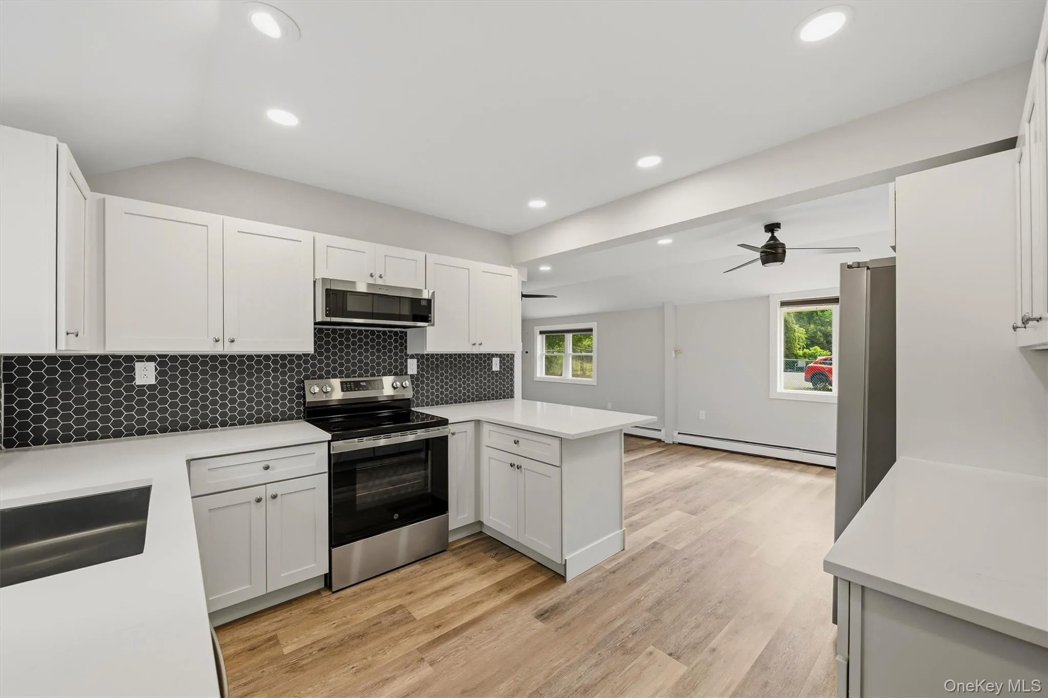 Modern kitchen featuring white cabinetry, stainless steel appliances including a gas range and built-in microwave, black subway tile backsplash, and wood-finish flooring Modern kitchen featuring white cabinetry, stainless steel appliances including a gas range and built-in microwave, black subway tile backsplash, and wood-finish flooring