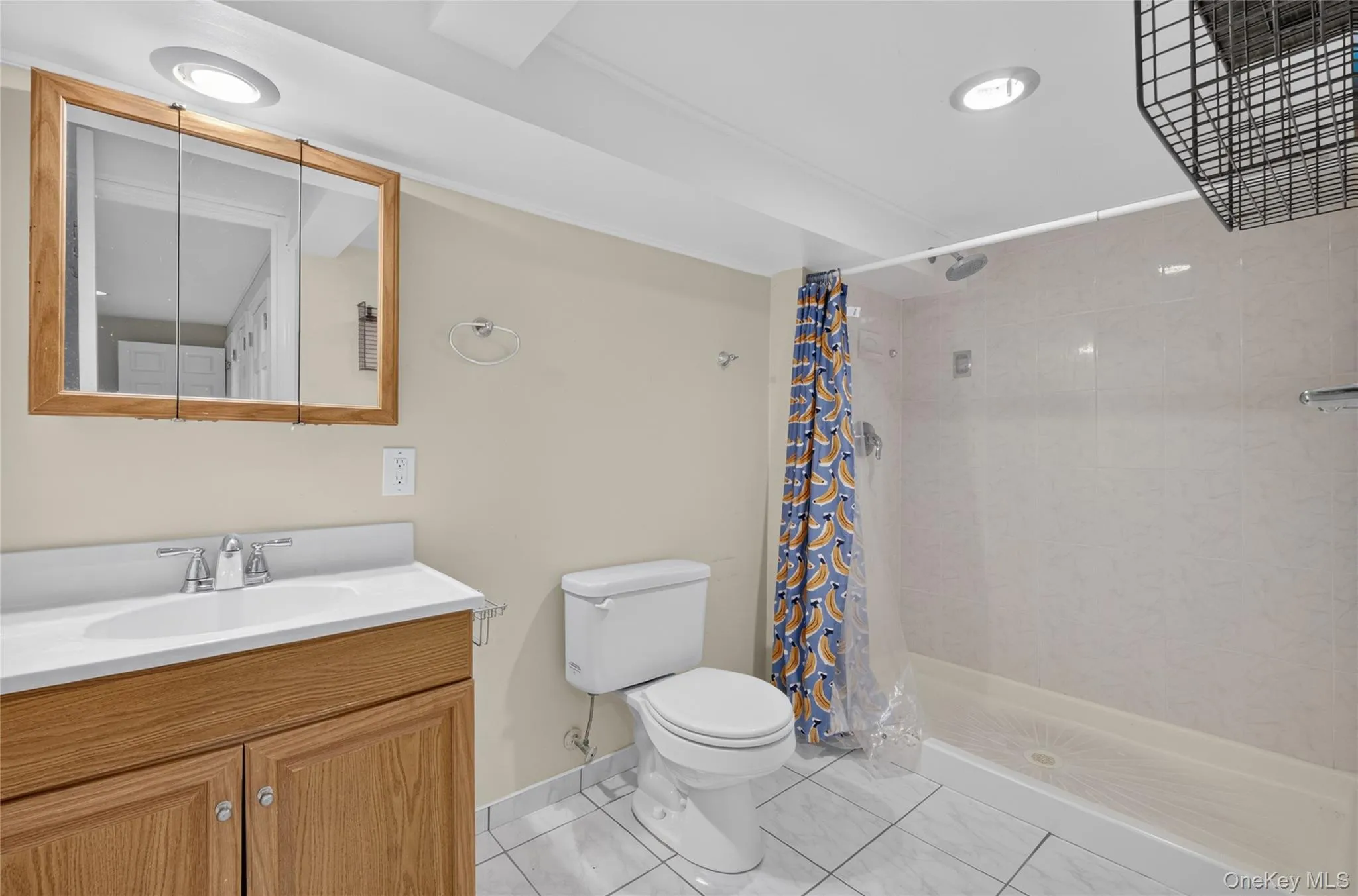 Bathroom featuring a vanity with a white countertop and wood-finish cabinetry, a framed mirrored medicine cabinet, a toilet, a tiled shower enclosure, and recessed lighting Bathroom featuring a vanity with a white countertop and wood-finish cabinetry, a framed mirrored medicine cabinet, a toilet, a tiled shower enclosure, and recessed lighting