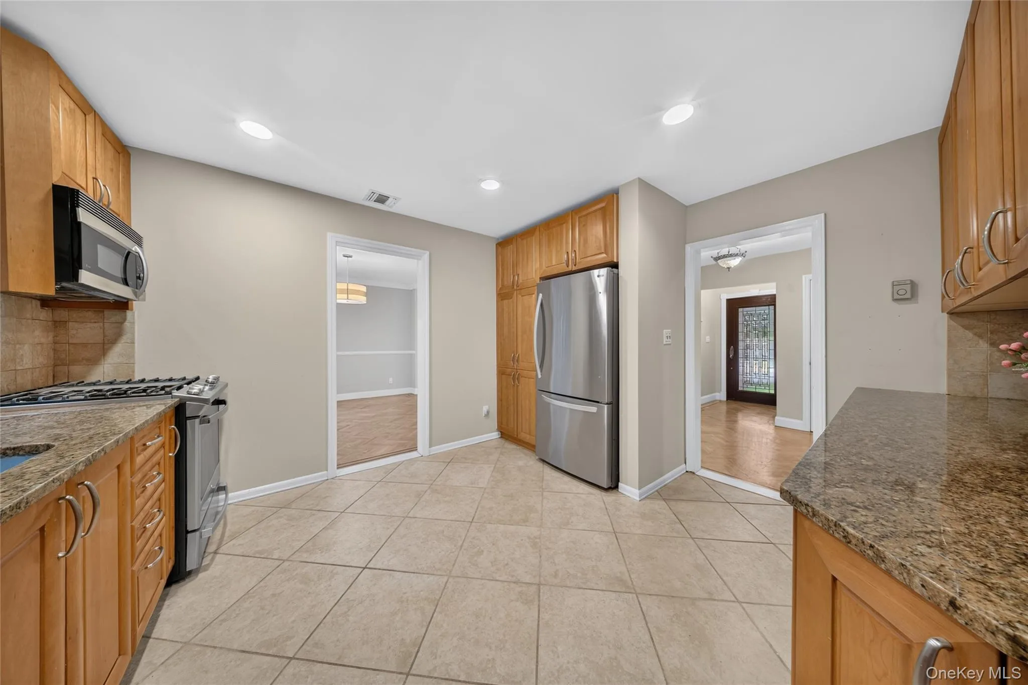 Kitchen featuring light wood cabinetry, granite-style countertops, stainless steel appliances, and a tile floor Kitchen featuring light wood cabinetry, granite-style countertops, stainless steel appliances, and a tile floor