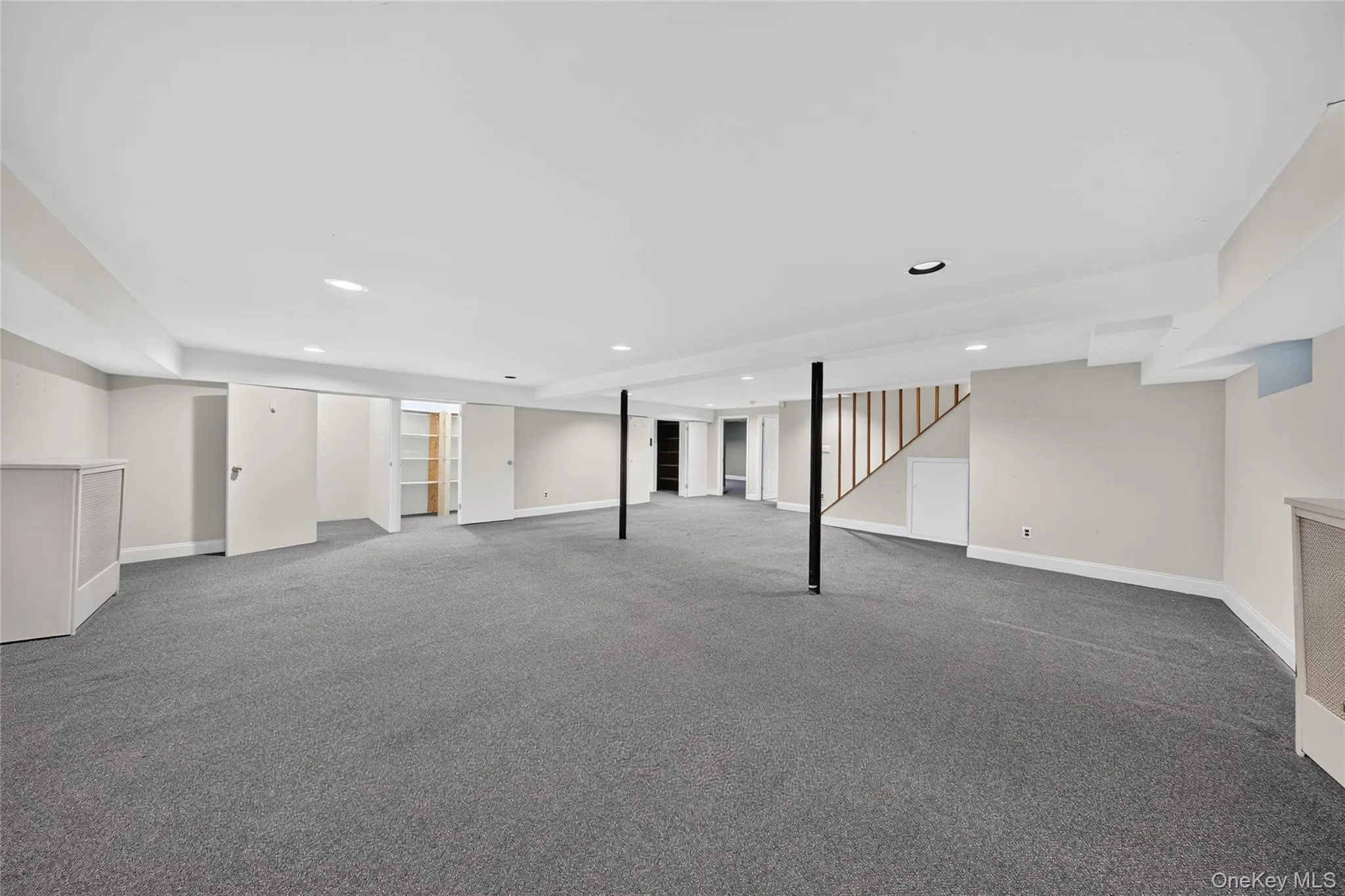 Spacious finished lower level featuring recessed lighting, gray carpeting, neutral wall colors, built-in shelving, and a visible staircase Spacious finished lower level featuring recessed lighting, gray carpeting, neutral wall colors, built-in shelving, and a visible staircase