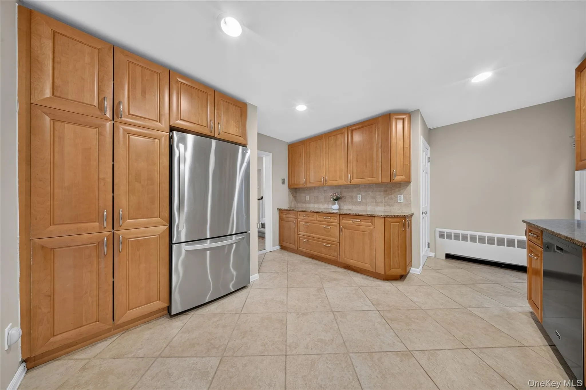 Kitchen featuring extensive light wood cabinetry, stainless steel refrigerator, tile flooring, granite-style countertops, and a tile backsplash Kitchen featuring extensive light wood cabinetry, stainless steel refrigerator, tile flooring, granite-style countertops, and a tile backsplash
