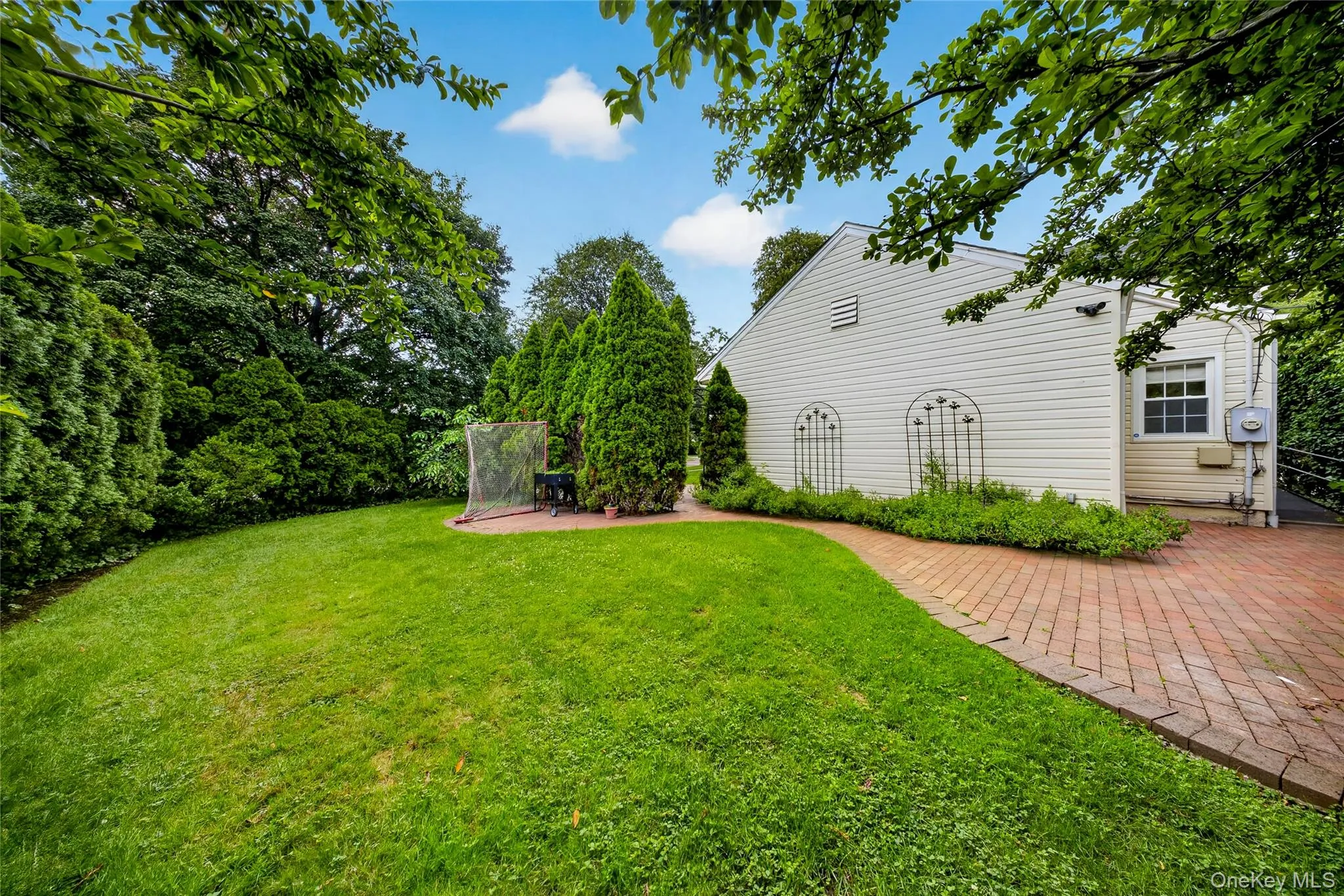Expansive rear yard featuring a brick paver patio, a lush lawn, mature trees, and established perimeter landscaping Expansive rear yard featuring a brick paver patio, a lush lawn, mature trees, and established perimeter landscaping