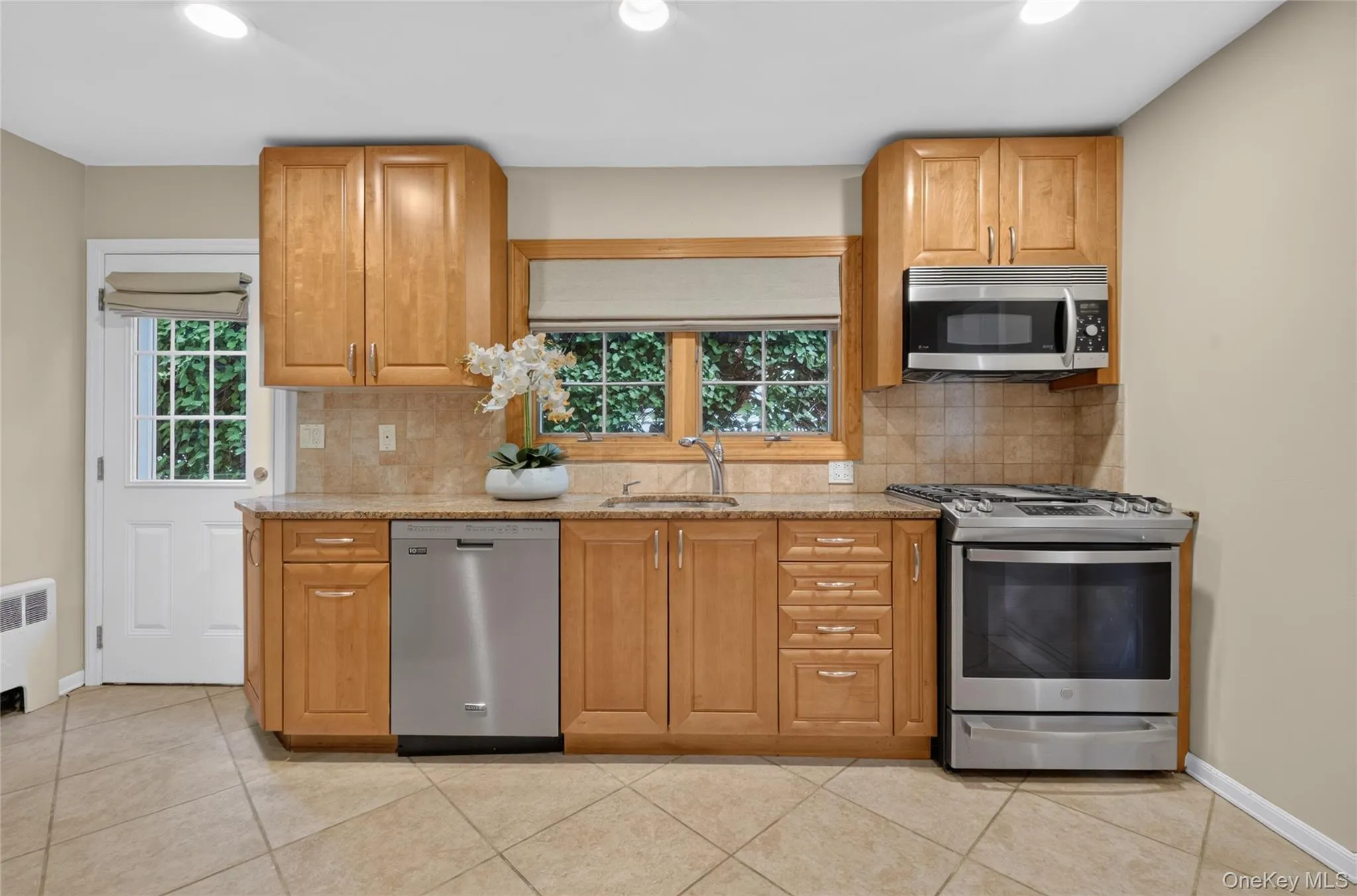 Kitchen featuring wood cabinetry, stone countertops, stainless steel appliances, and a tile backsplash Kitchen featuring wood cabinetry, stone countertops, stainless steel appliances, and a tile backsplash