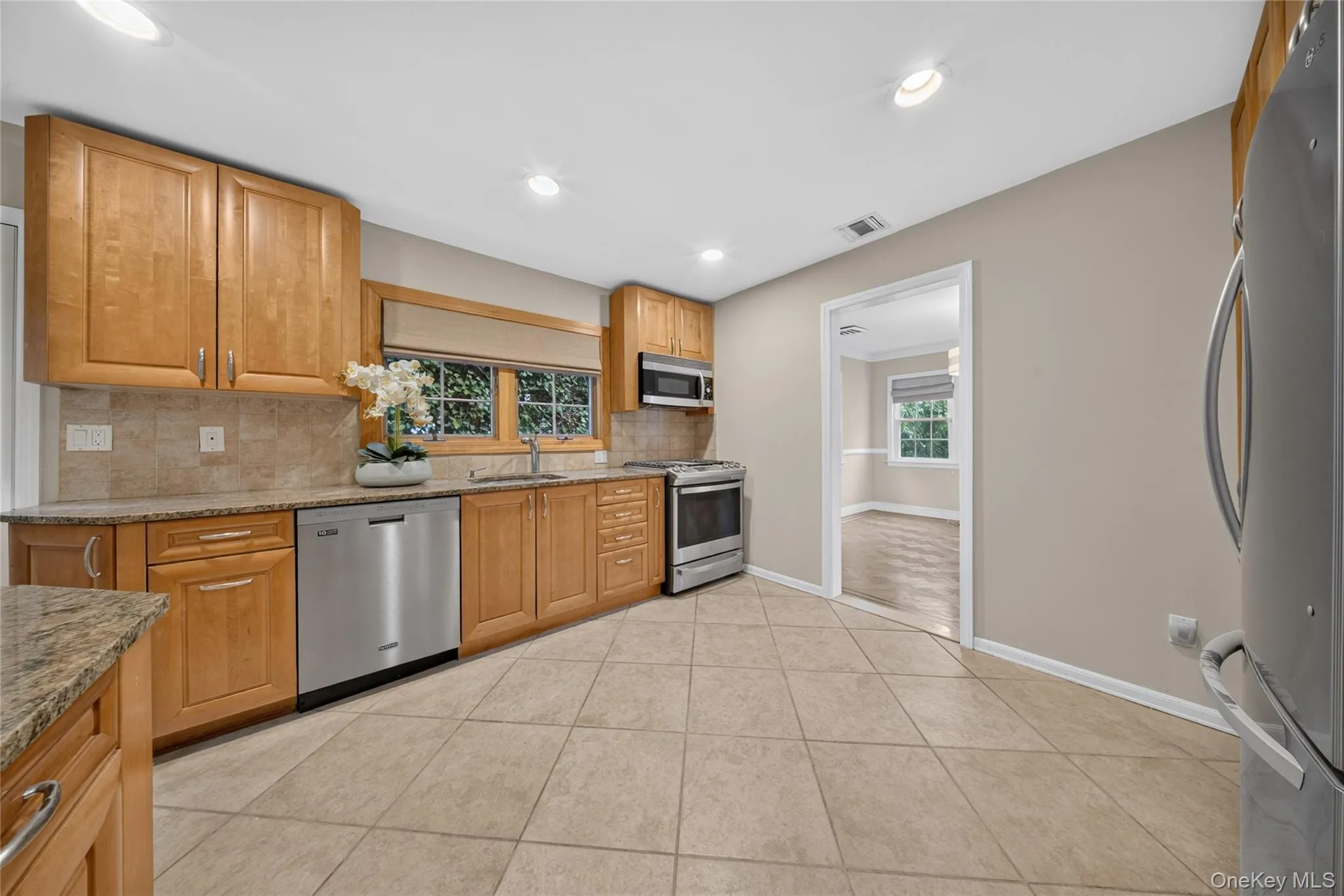 Kitchen featuring light wood cabinetry with stainless steel appliances, granite countertops, and a tile backsplash Kitchen featuring light wood cabinetry with stainless steel appliances, granite countertops, and a tile backsplash