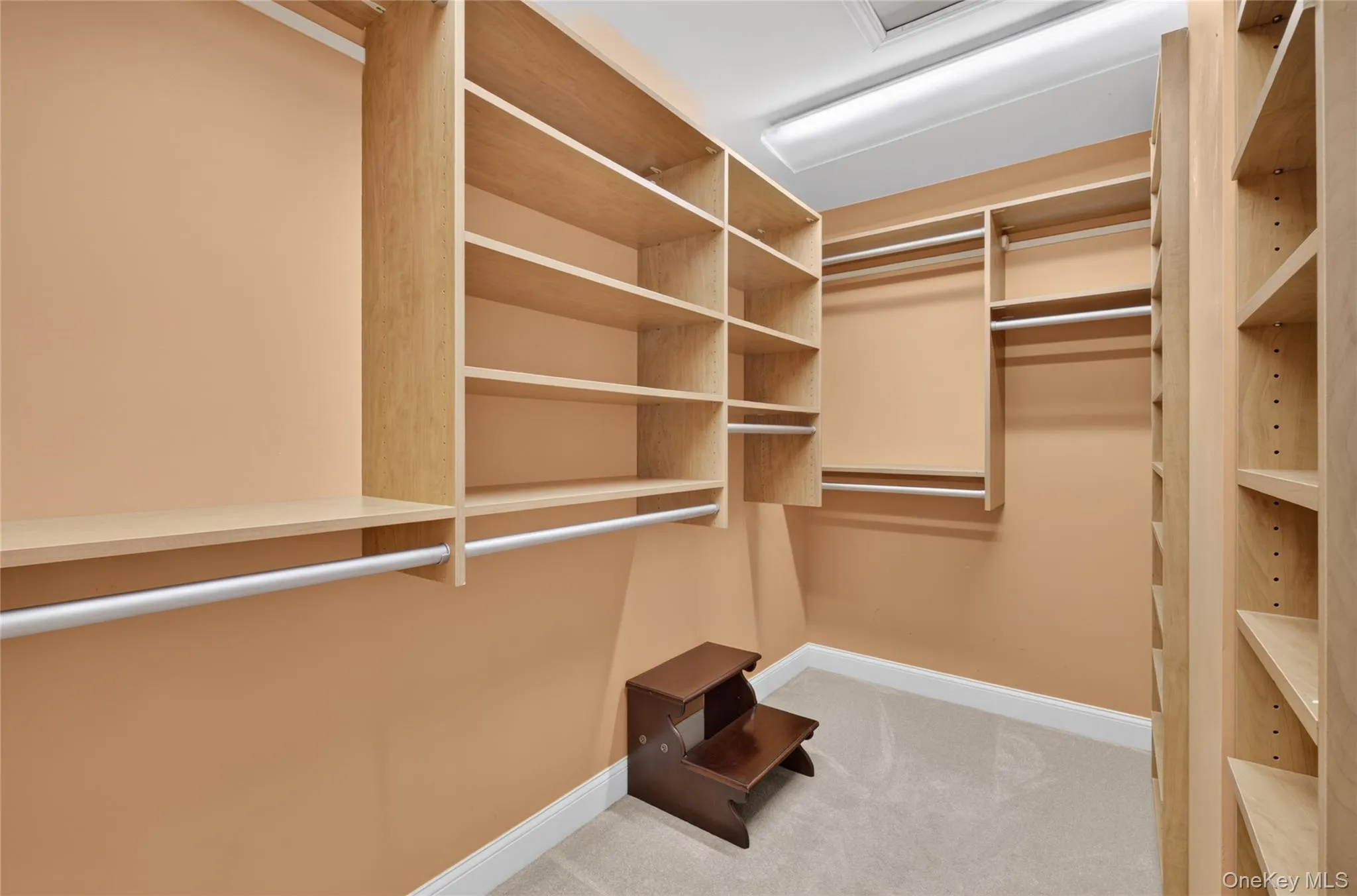 Custom walk-in closet featuring extensive built-in shelving, multiple hanging rods, warm-toned walls, and soft carpet flooring Custom walk-in closet featuring extensive built-in shelving, multiple hanging rods, warm-toned walls, and soft carpet flooring